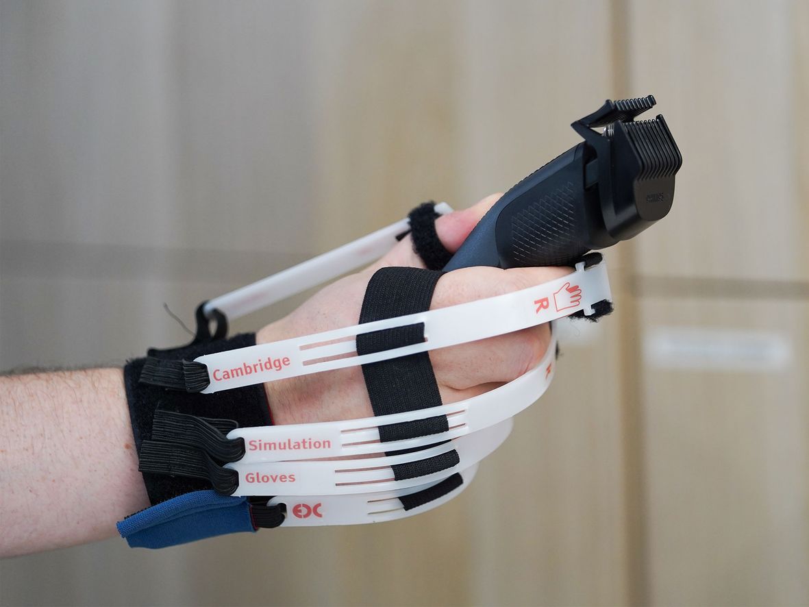 Person's arm with a specialized glove holding a black beard trimmer, featuring white straps and labels.