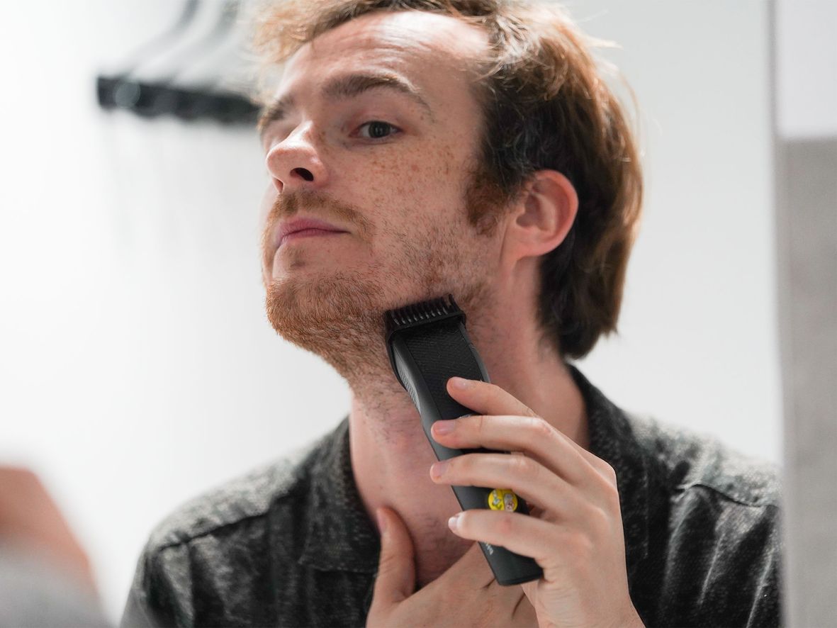 Man with short hair and beard using a black beard trimmer on his neck.