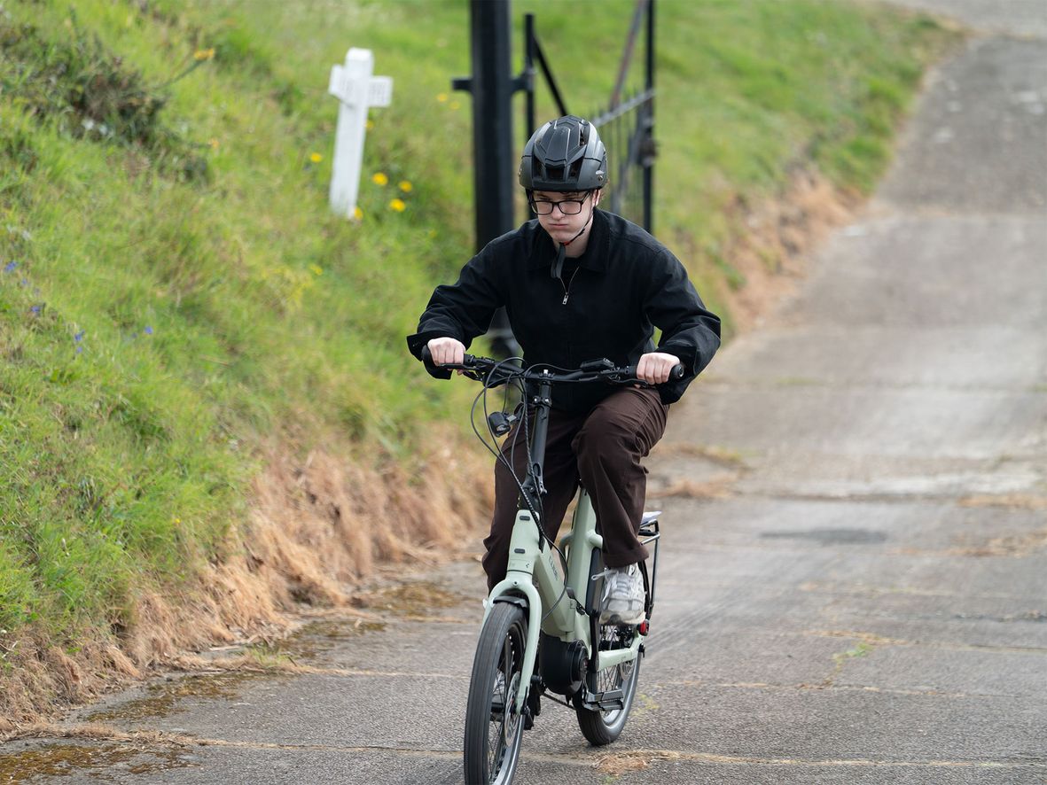 Person in black jacket, brown pants, and helmet rides a light green bicycle on a paved path.
