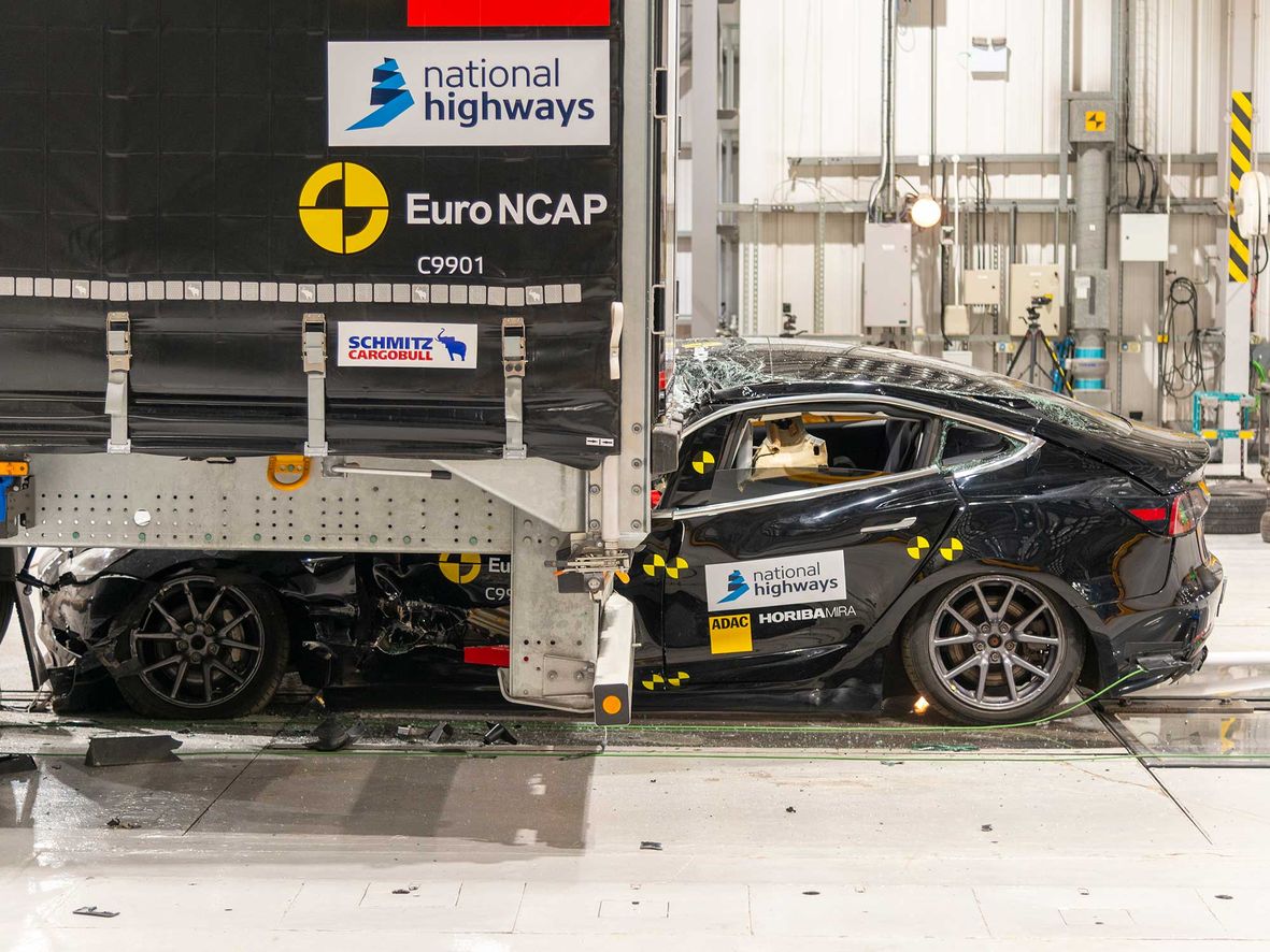 A Tesla Model 3 being crashed into the back of a lorry fitted with the current UK standard of rear underrun protection. The passenger compartment is crushed under the lorry.