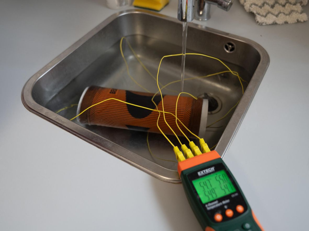 A person is using a multi-meter to measure the temperature of water in a sink. In the sink is a knee support stretched on a tube
