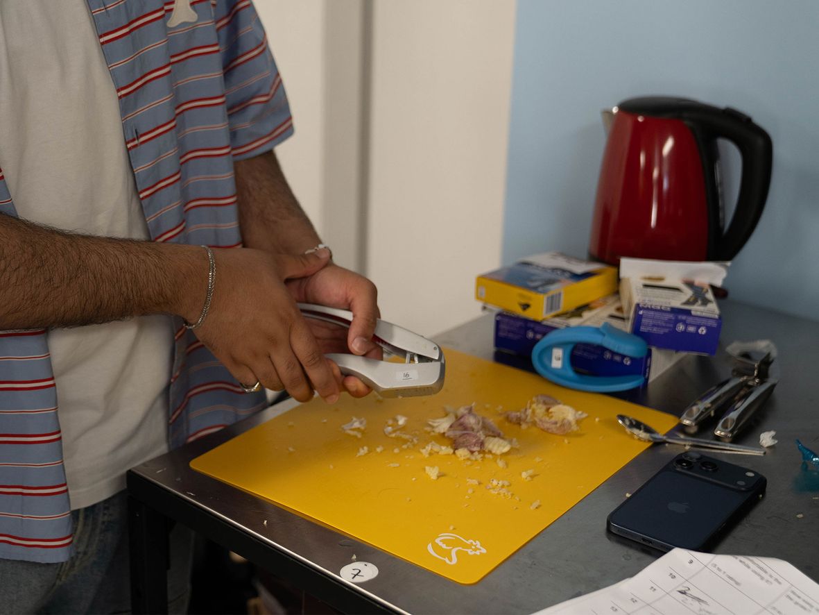 Person in striped shirt using garlic press on yellow cutting board, surrounded by kitchen items.