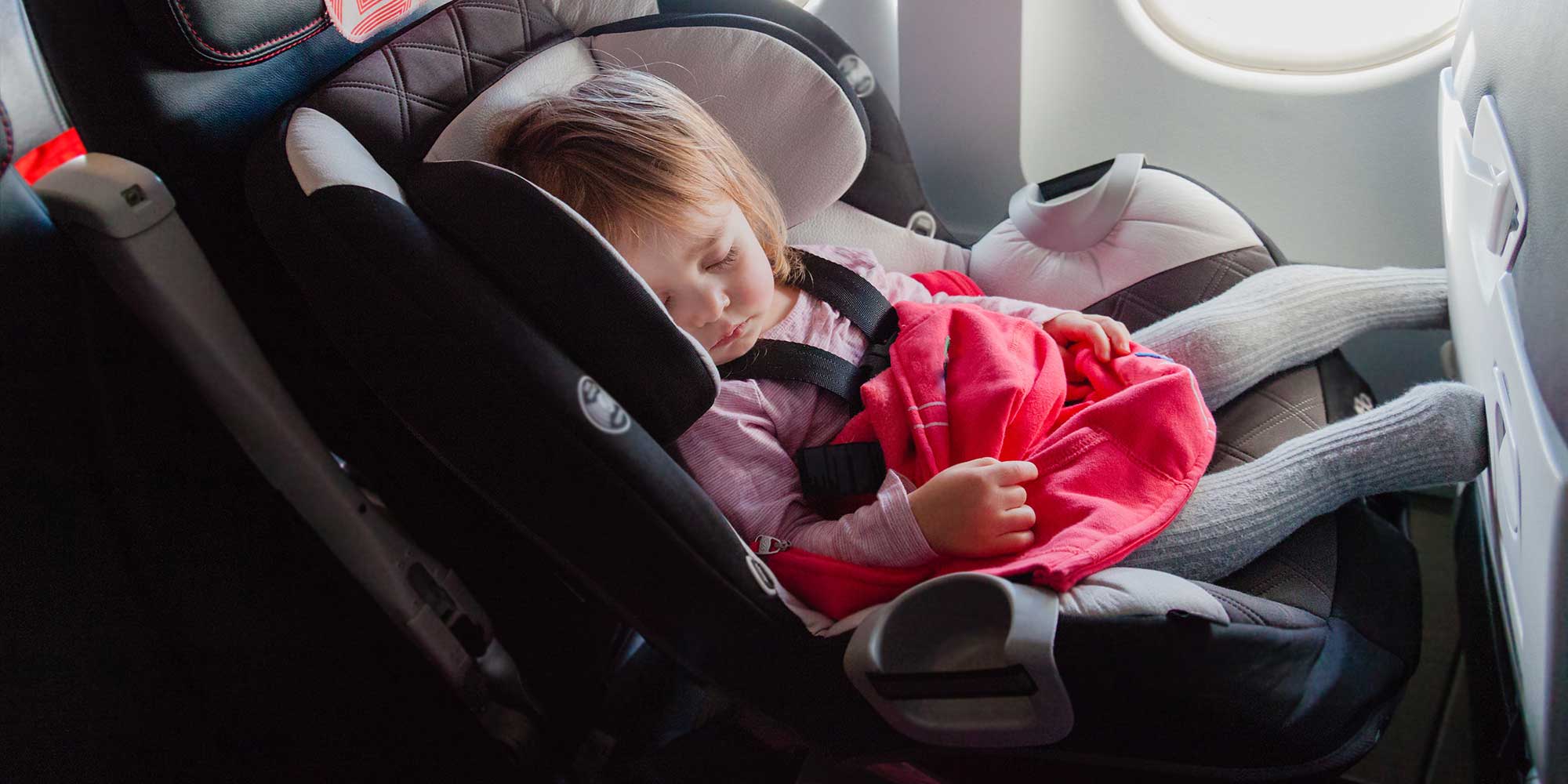 A baby asleep in a car seat on a plane