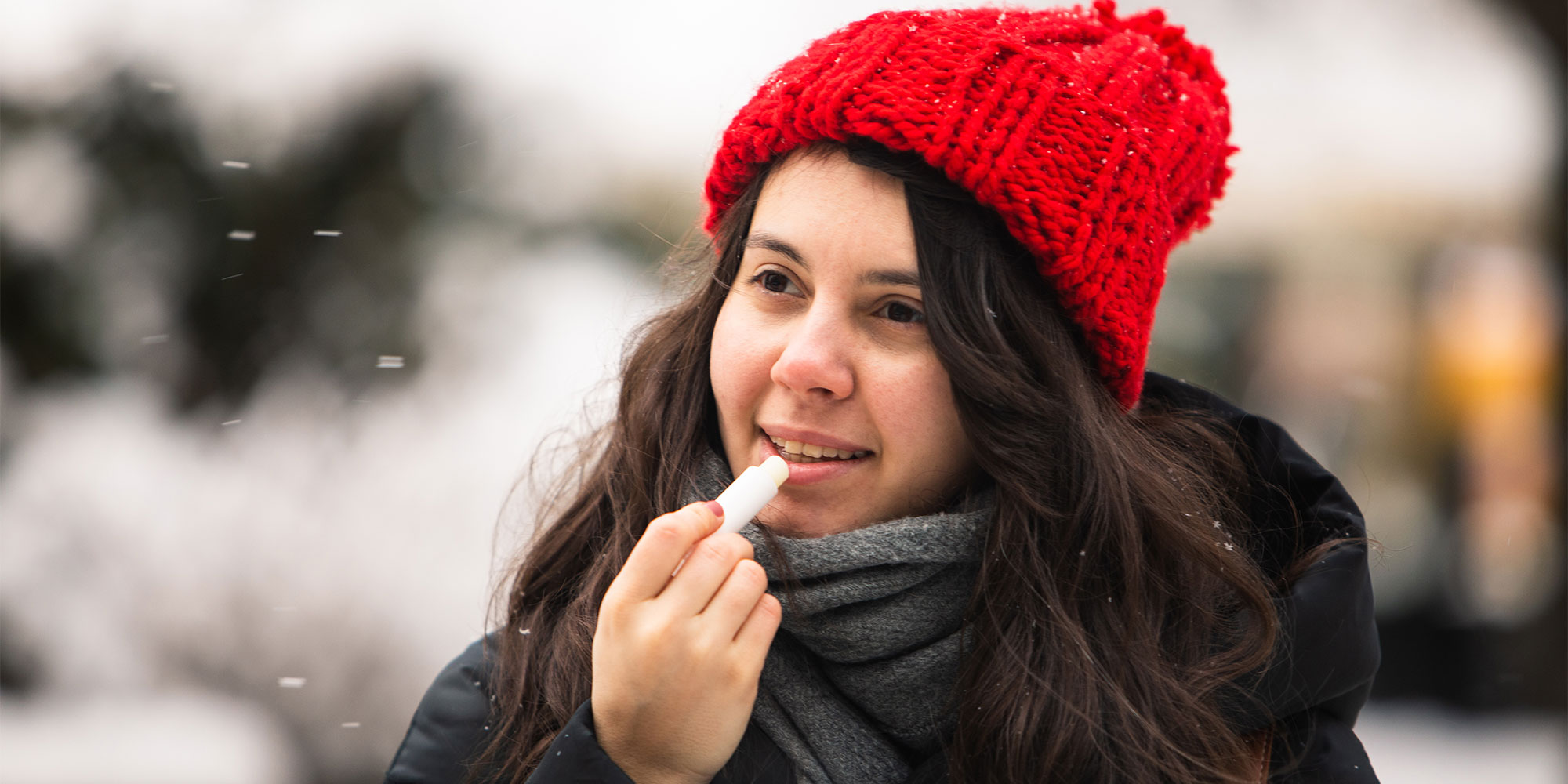 Woman outdoors with a woolly hat on applying lip balm