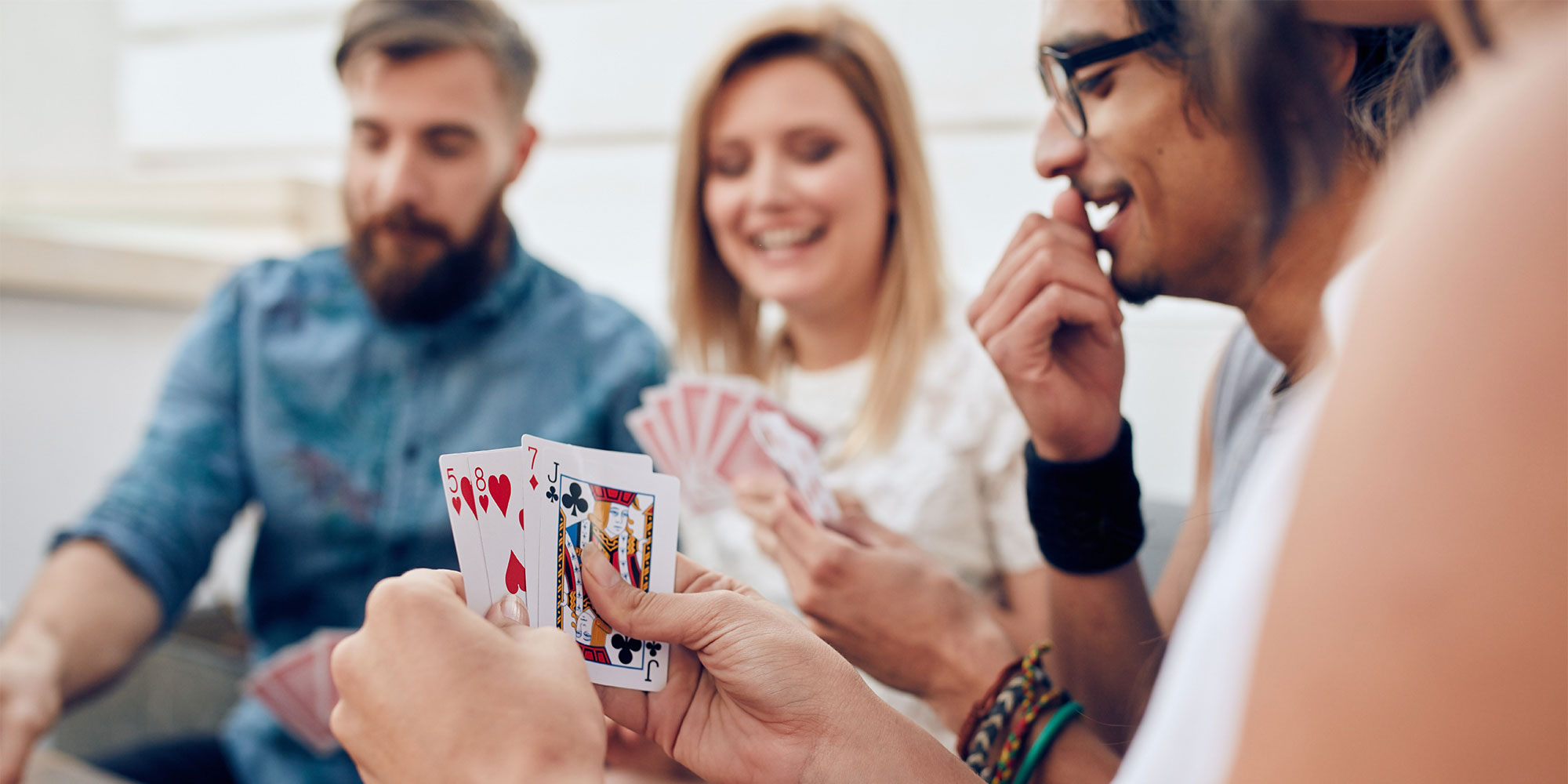 Four people sitting around a table playing cards. One person holds three cards, another holds two.