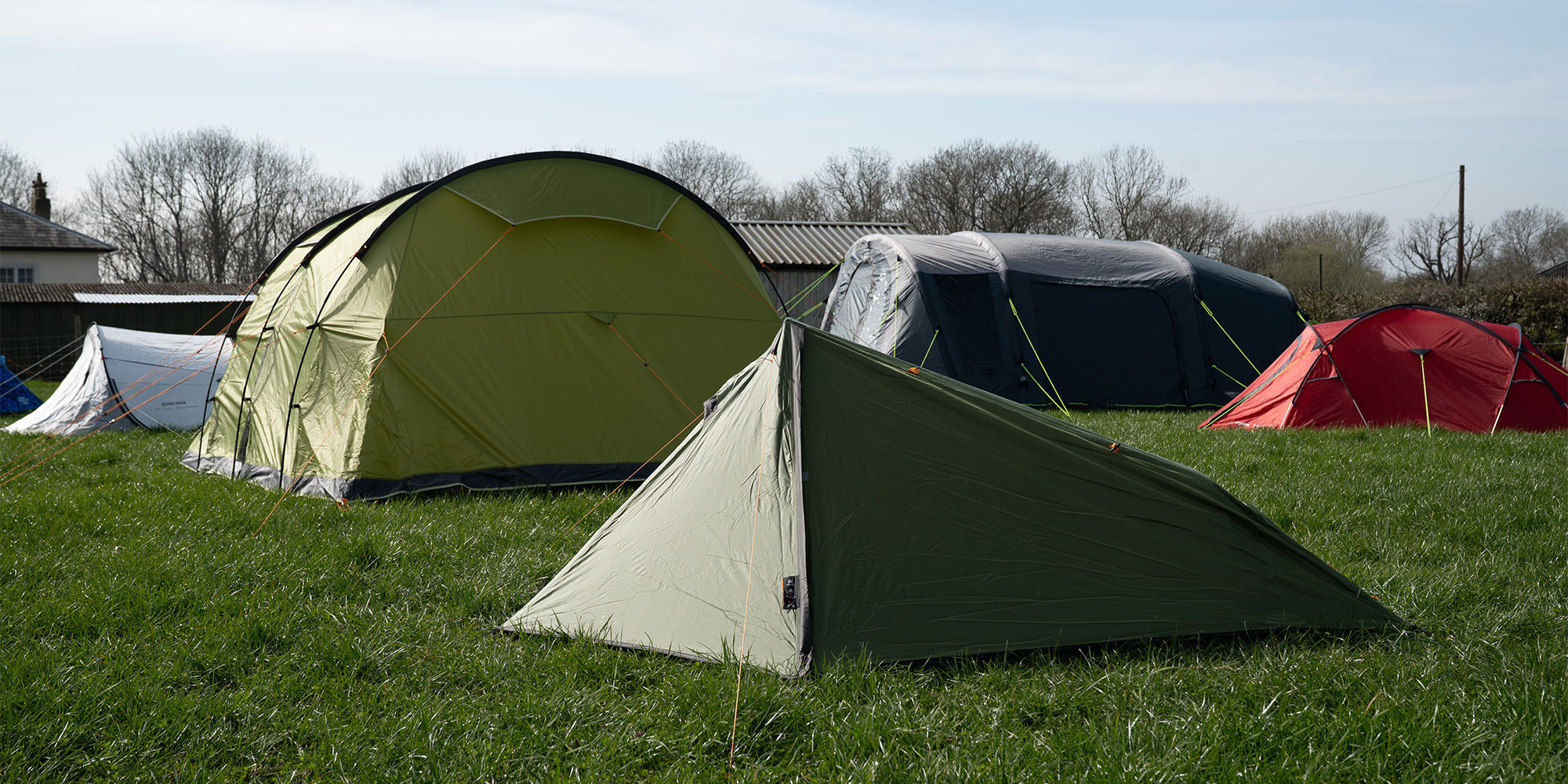 Several tents of various colors and sizes are pitched on a grassy field.