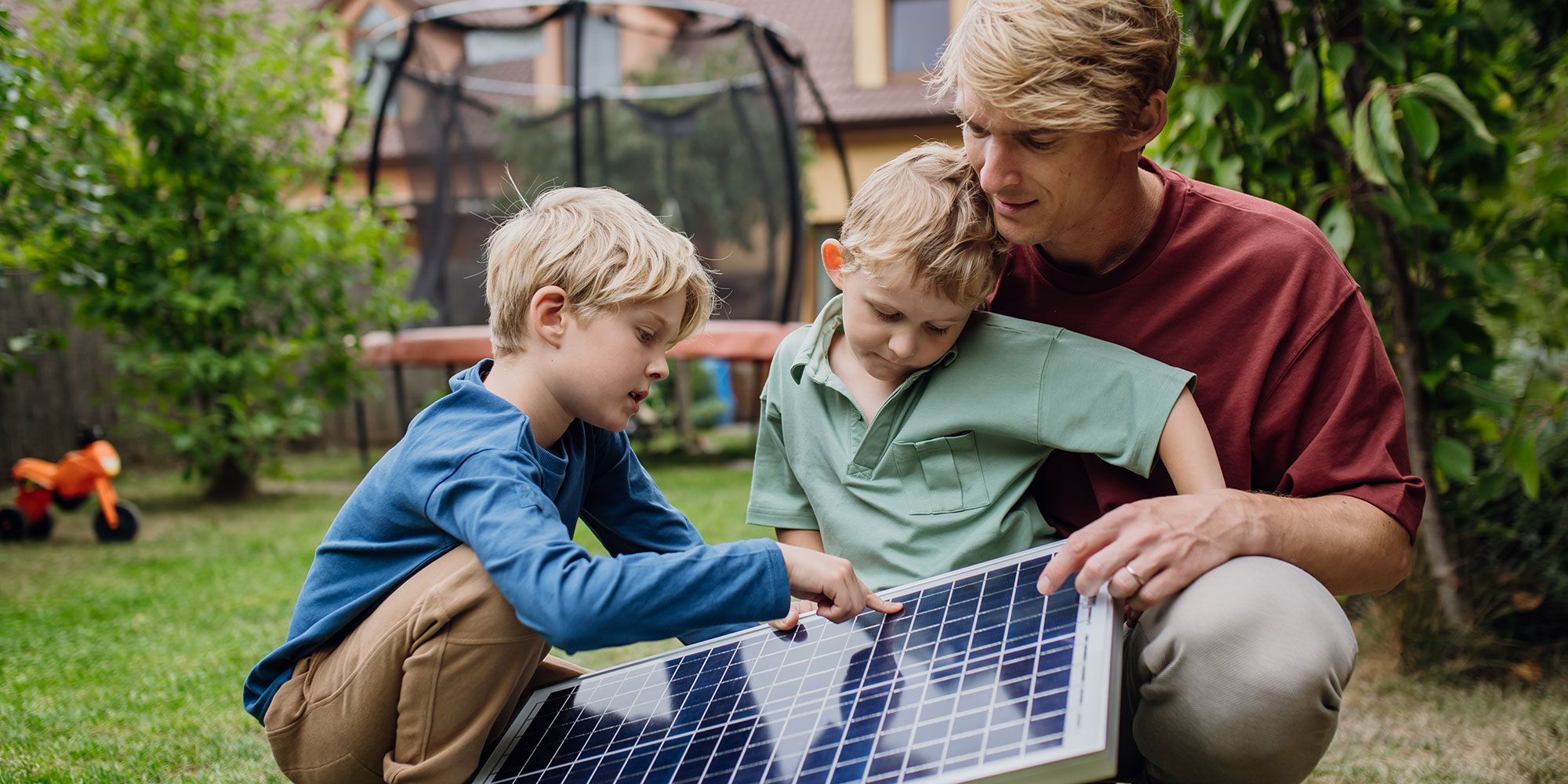Two children and father looking at a solar panel in a family garden