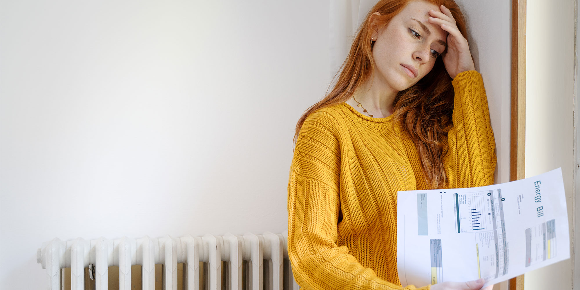 Red-headed woman in yellow jumper looking anxious with an energy bill