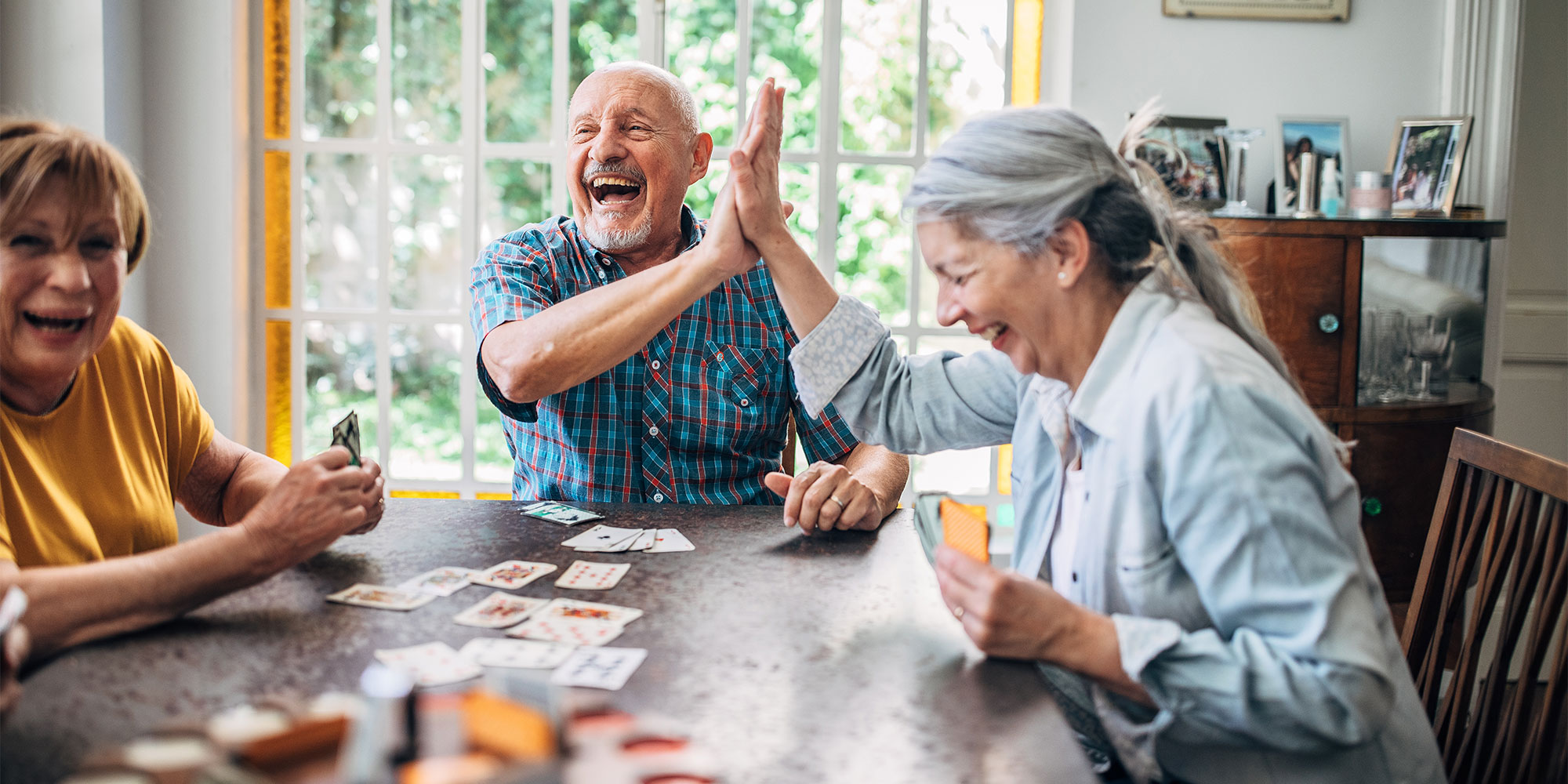 Three people sit at a table playing cards. A man and woman laugh and give each other high fives.