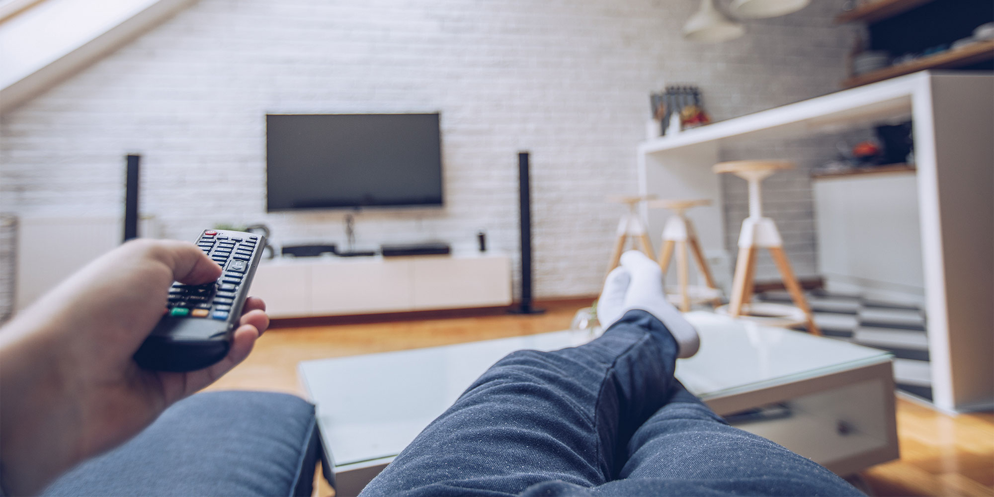 Person holding a remote pointed at a TV in the distance on a wall