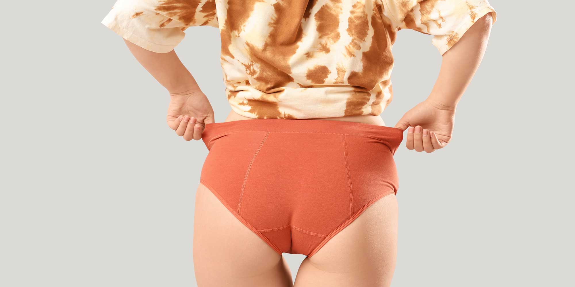 Woman in orange underwear and tie-dye top, hands on hips, facing away.