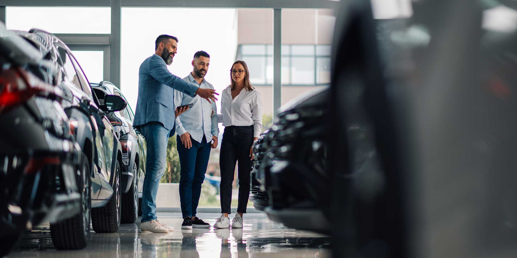 A man shows two customers car in a showroom.