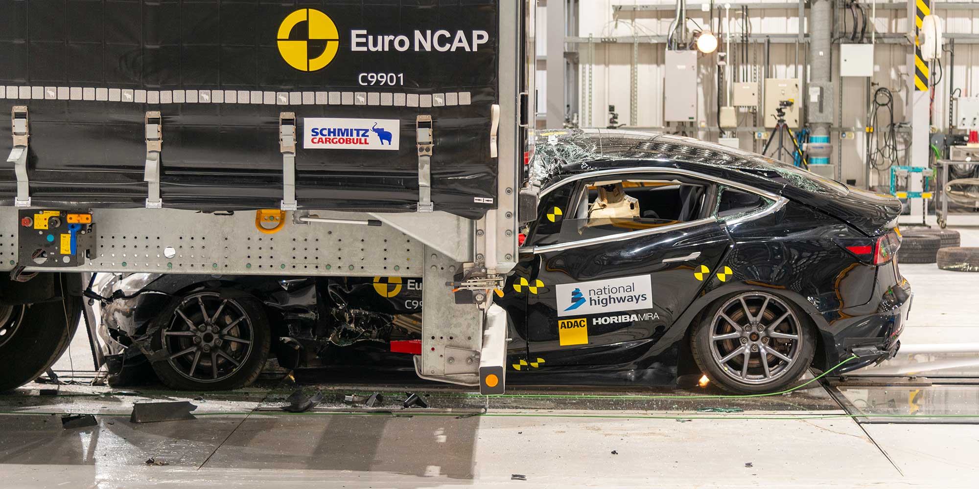 A Tesla Model 3 being crashed into the back of a lorry fitted with the current UK standard of rear underrun protection. The passenger compartment is crushed under the lorry.