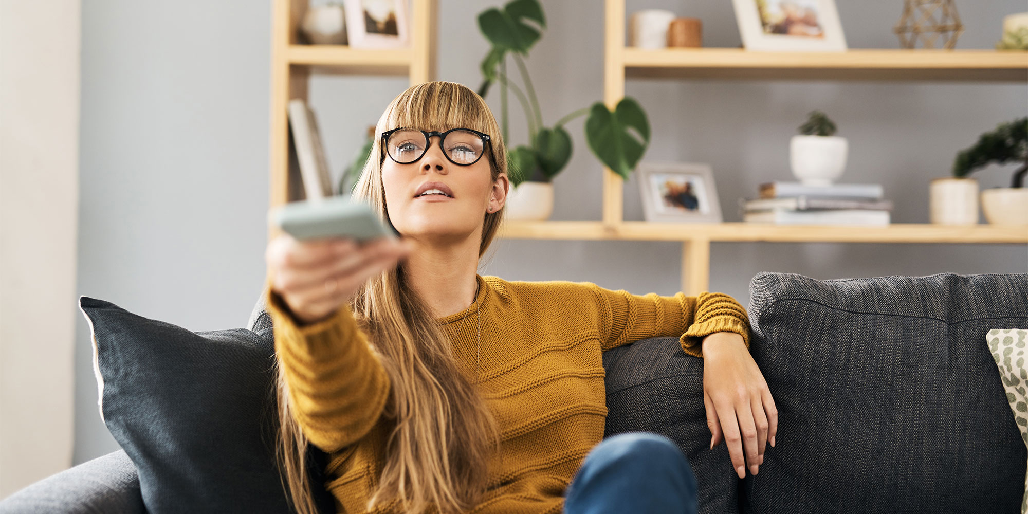 A woman holding a remote control towards the camera - she is changing the channel on the TV