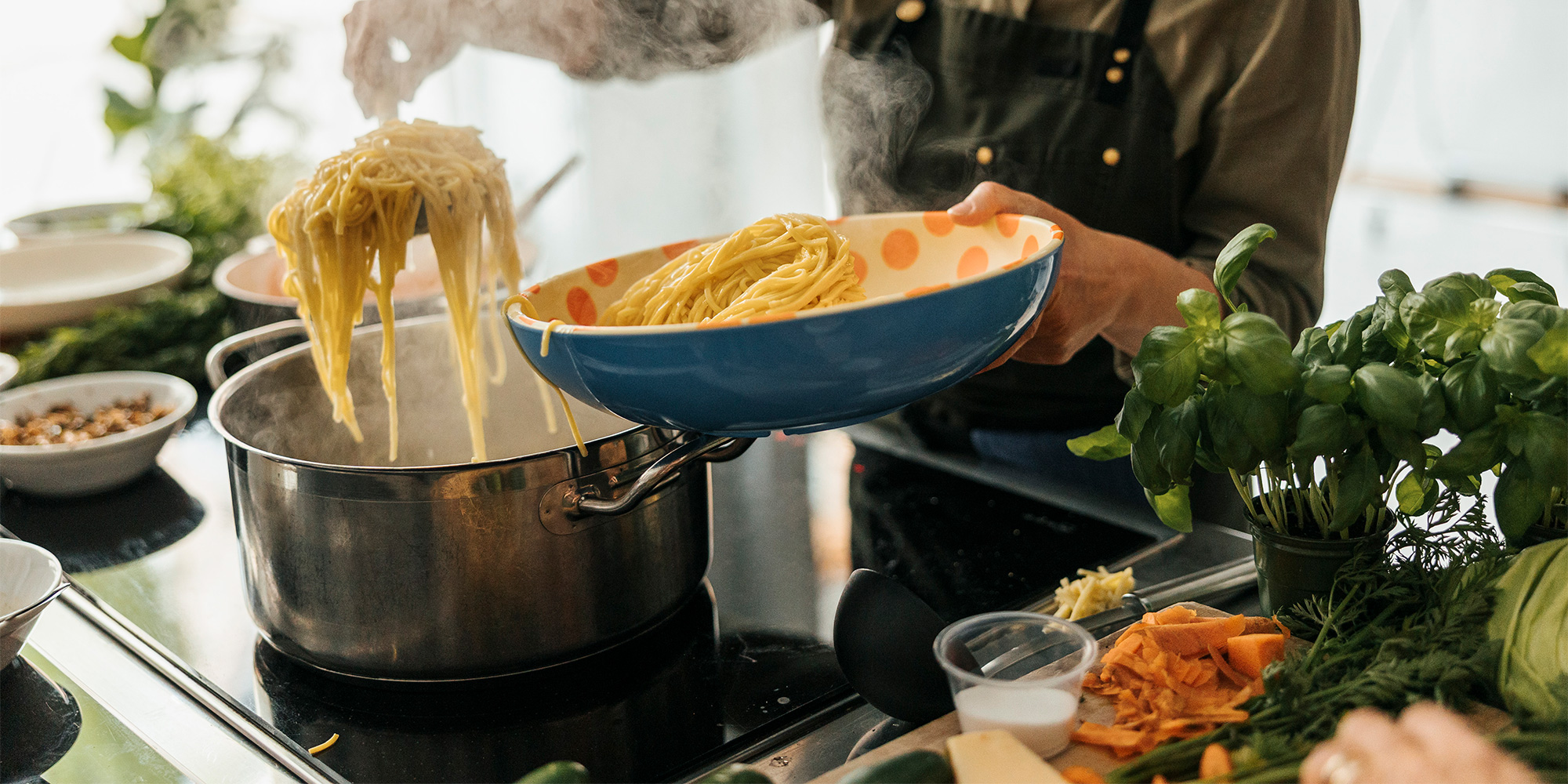 Spooning pasta from a pan on an induction hob