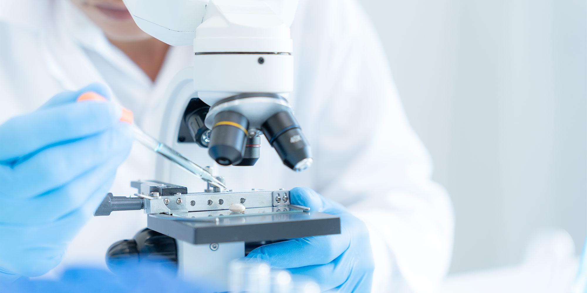 A microsope in a lab setting, being used by someone in a white medical coat