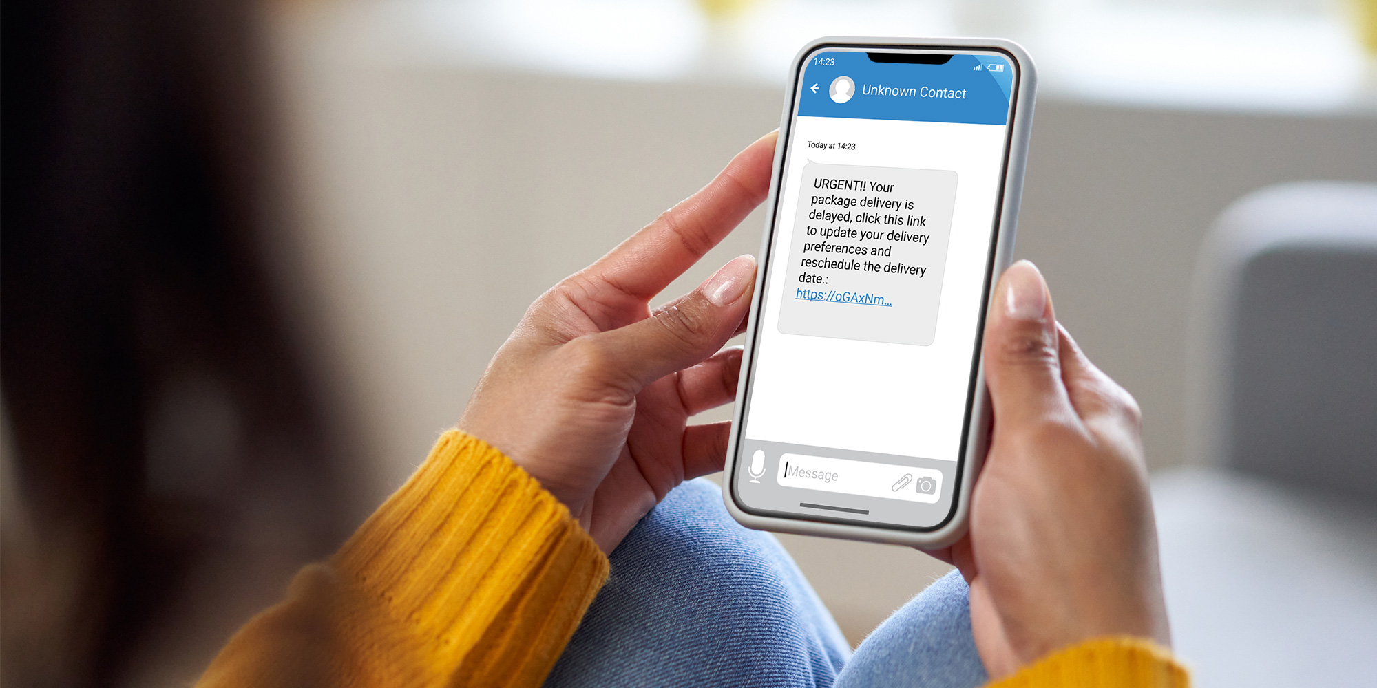 Woman in yellow jumper holds a mobile showing a fake text message