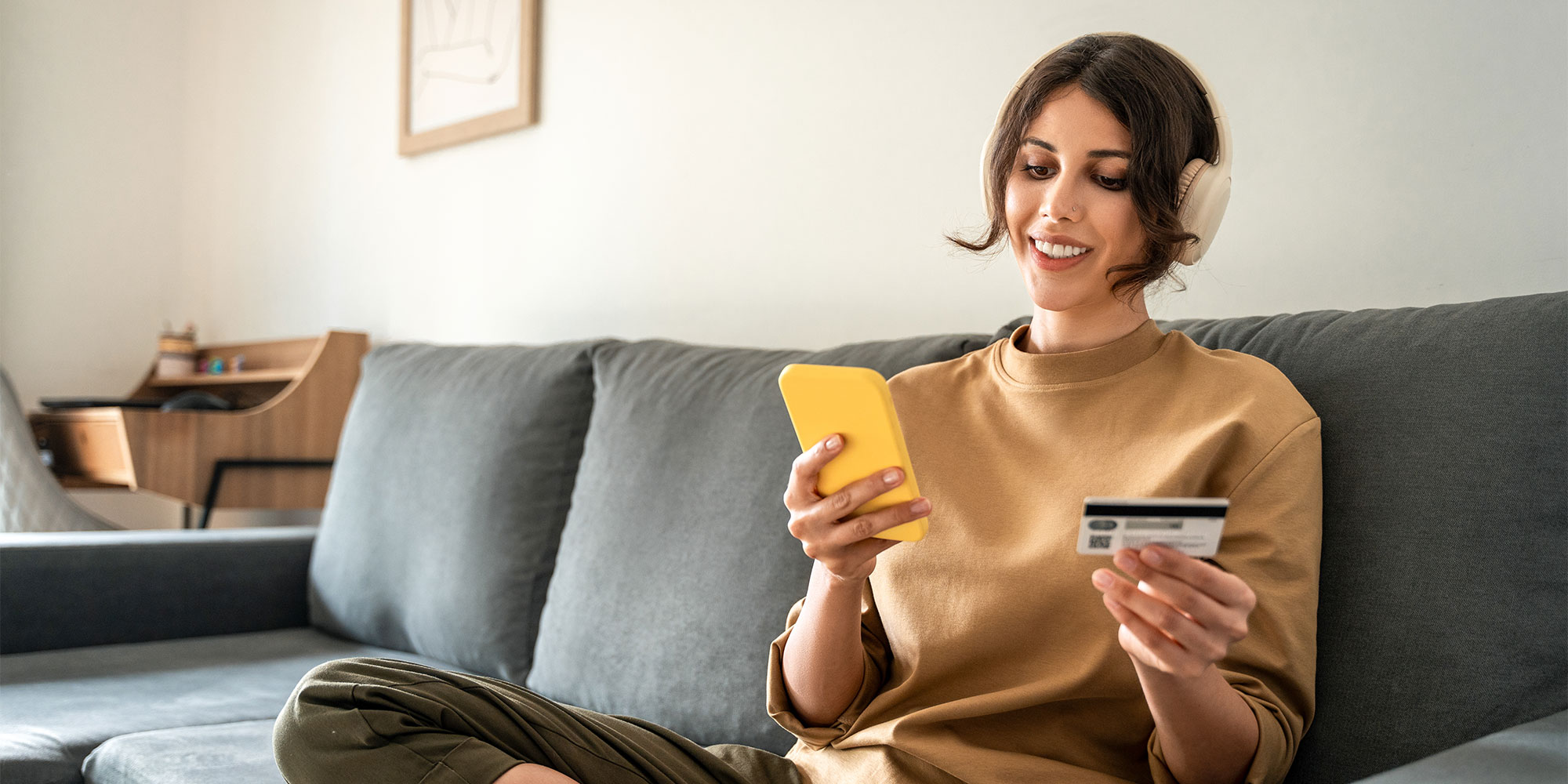 A woman sat on a grey sofa, ordering an item on her phone using her card