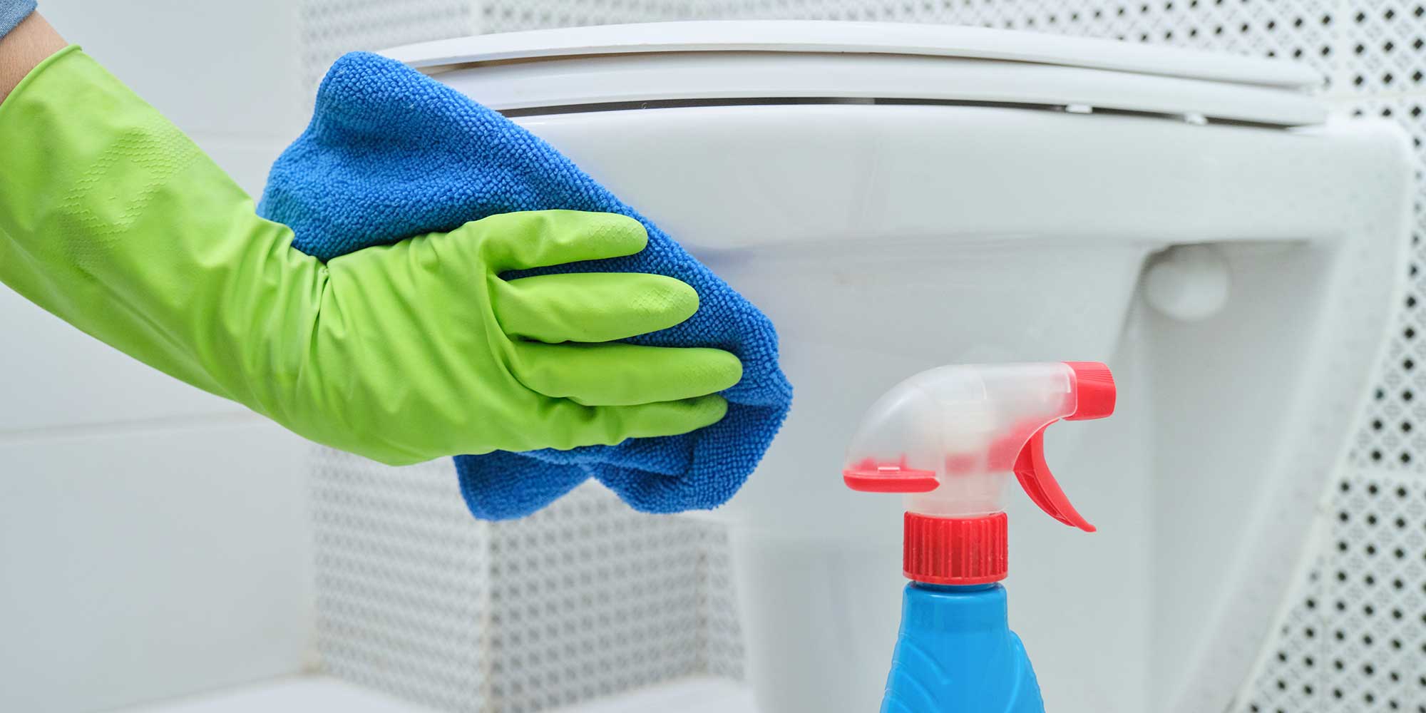 A white toilet being cleaned by someone wearing a green glove.