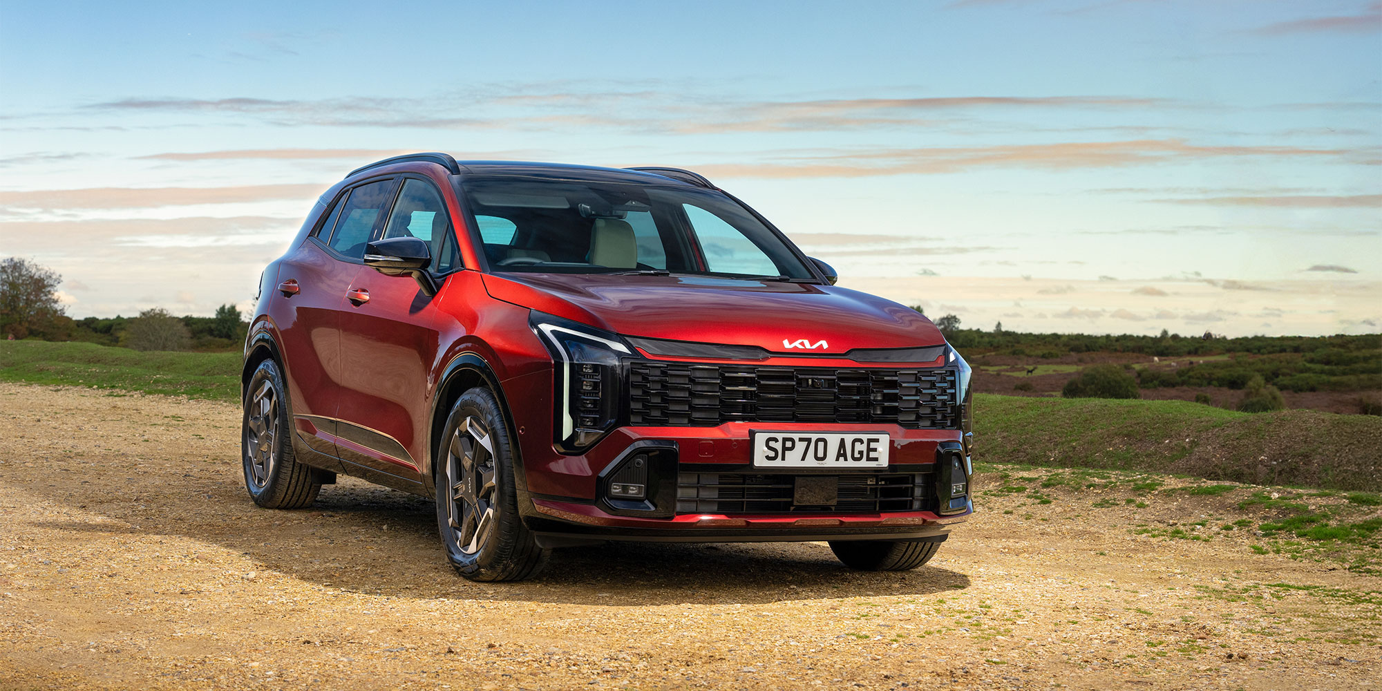 Red Kia Sportage SUV parked on a dirt road.