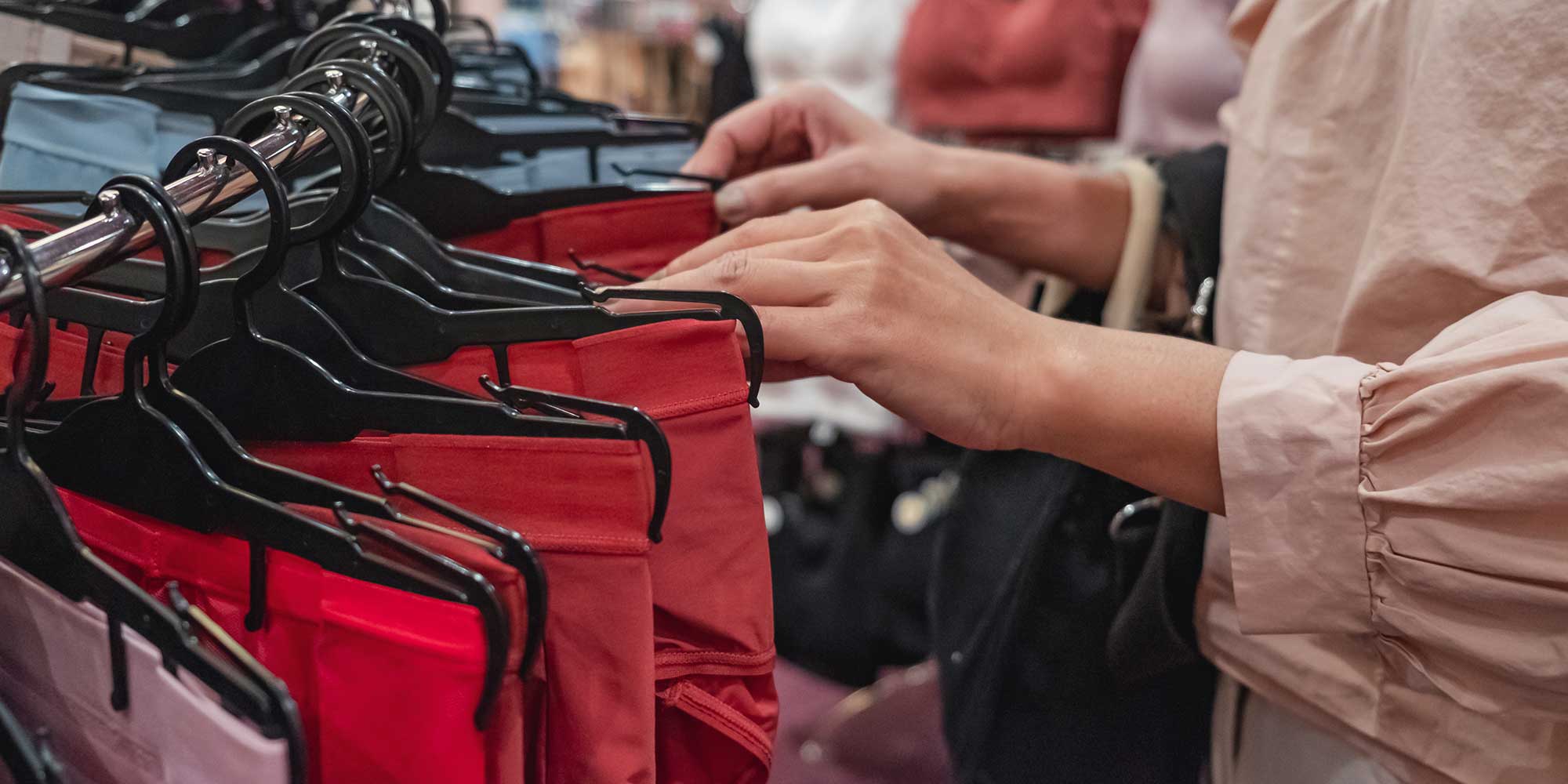 Person in a pink blouse browsing red period pants on a rack in a store.