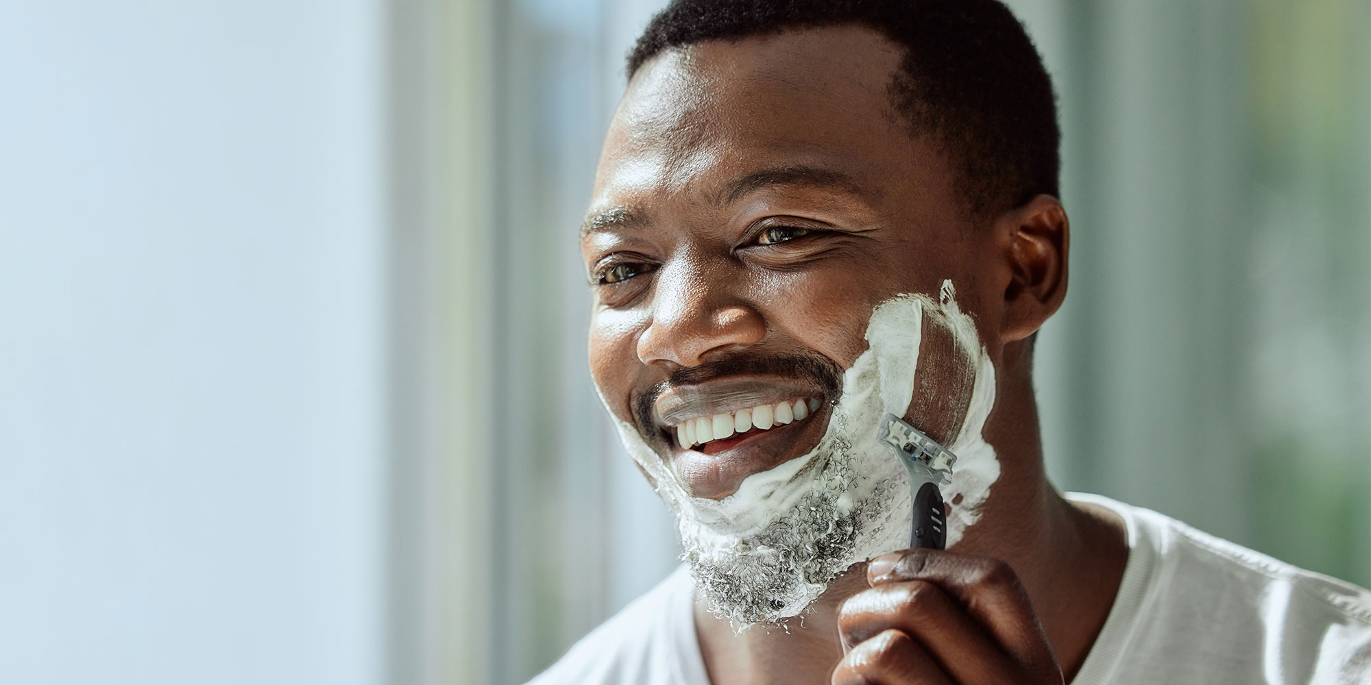 Black man shaving with a razor and foam on their face