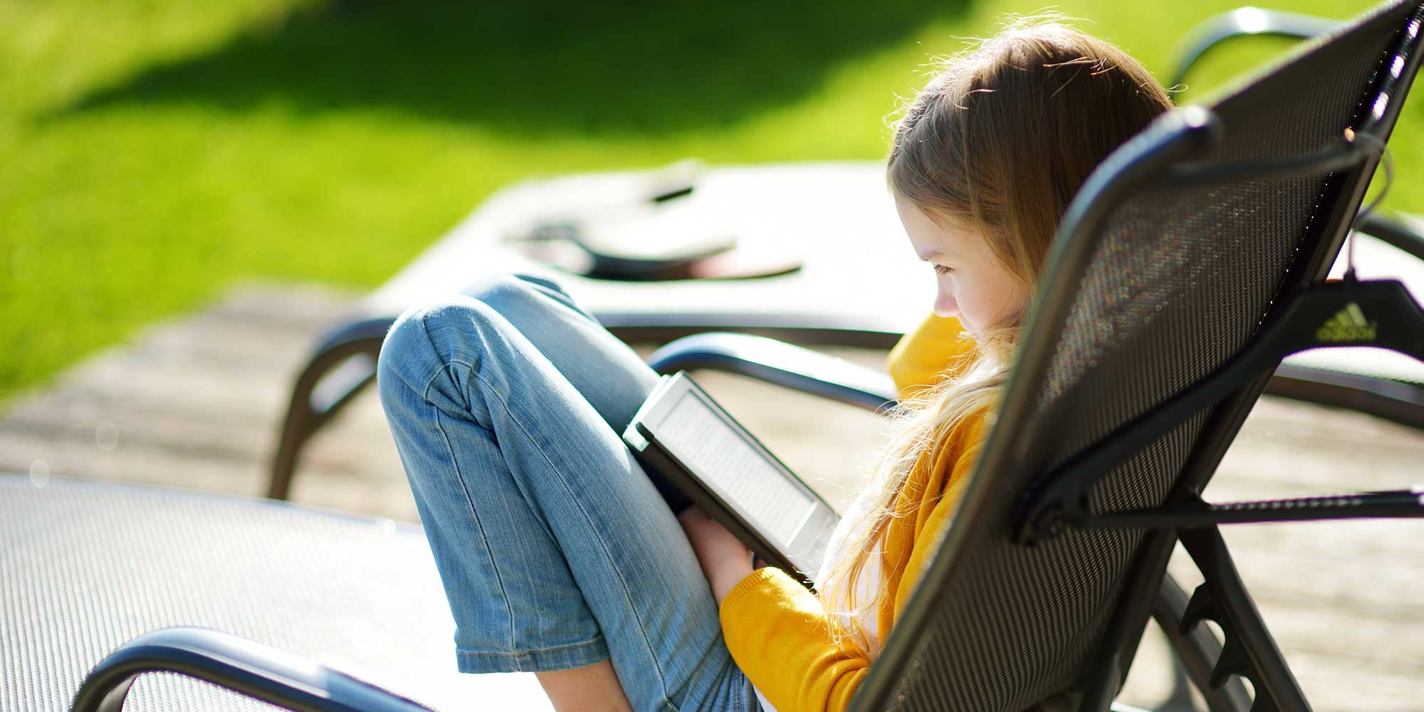 Child reading from an e-reader (ebook reader) outside.