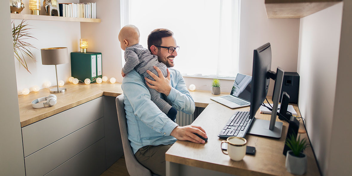 Man holding baby while working in home office