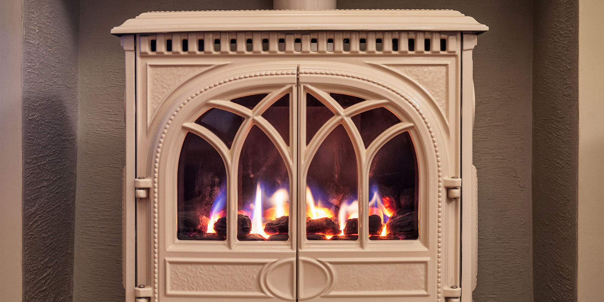 White wood-burning stove with arched glass doors, displaying blue and orange flames inside.