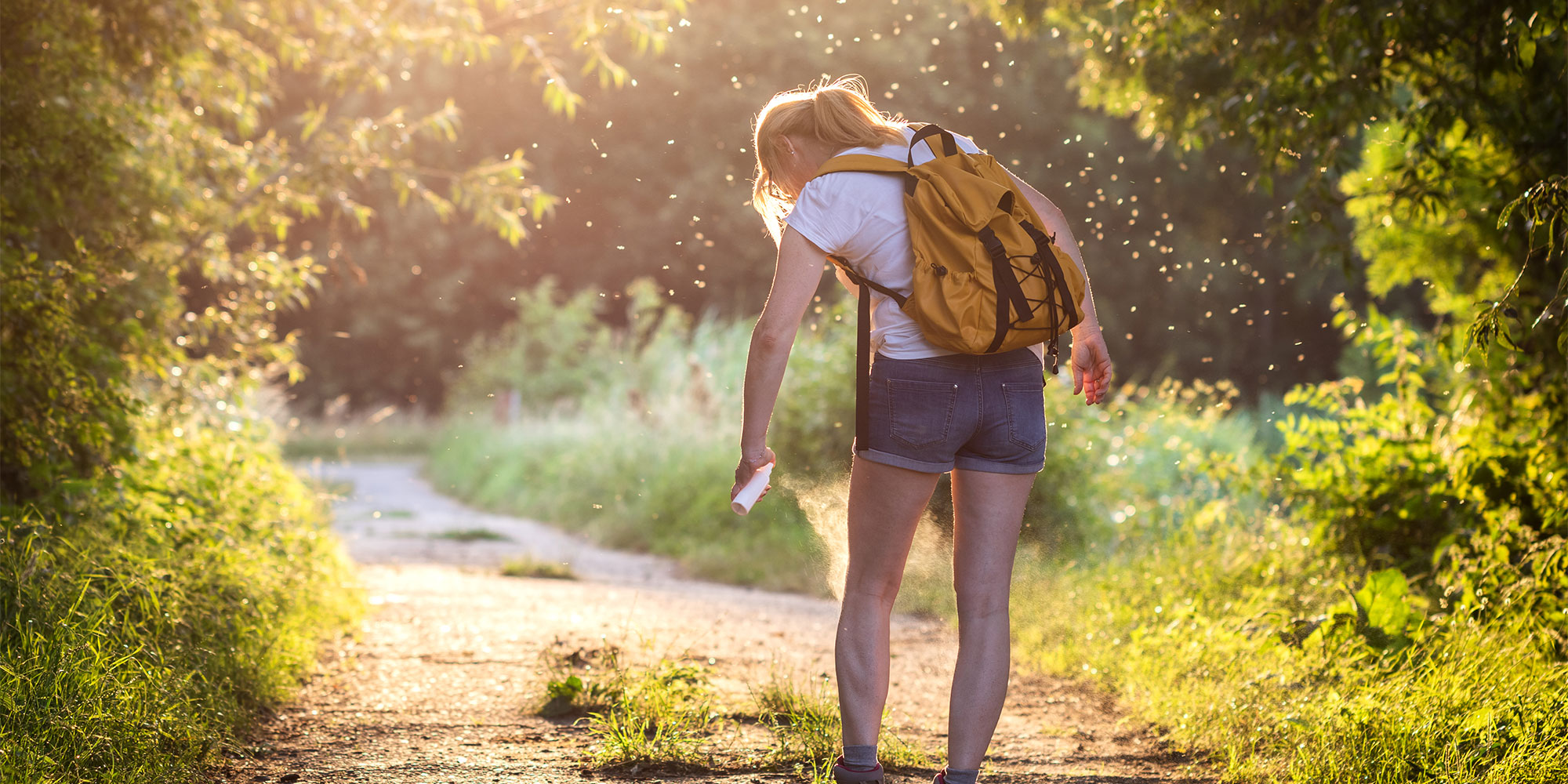 A woman spraying mosquito repellent onto her leg on a sunny day in the countryside.