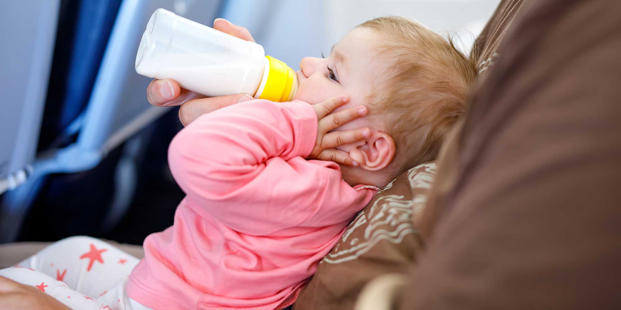 A baby drinking from a bottle on a plane