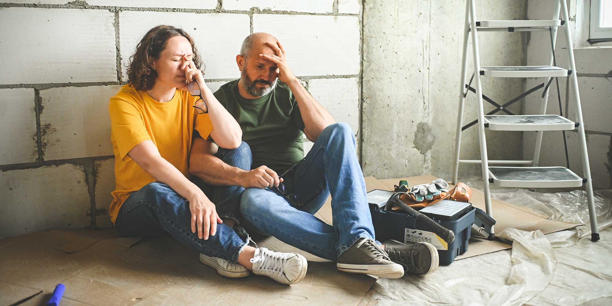 A man and a woman look upset while sitting on the floor of a building undergoing building work