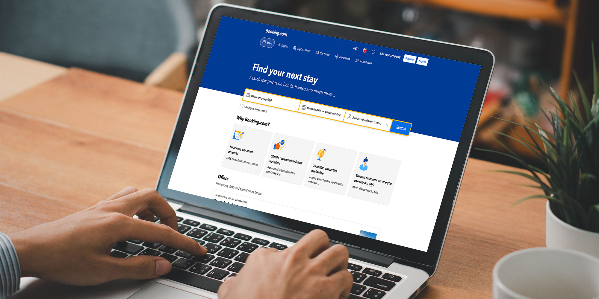 Hands hover on the keyboard of a laptop. The screen displays the Booking.com website.