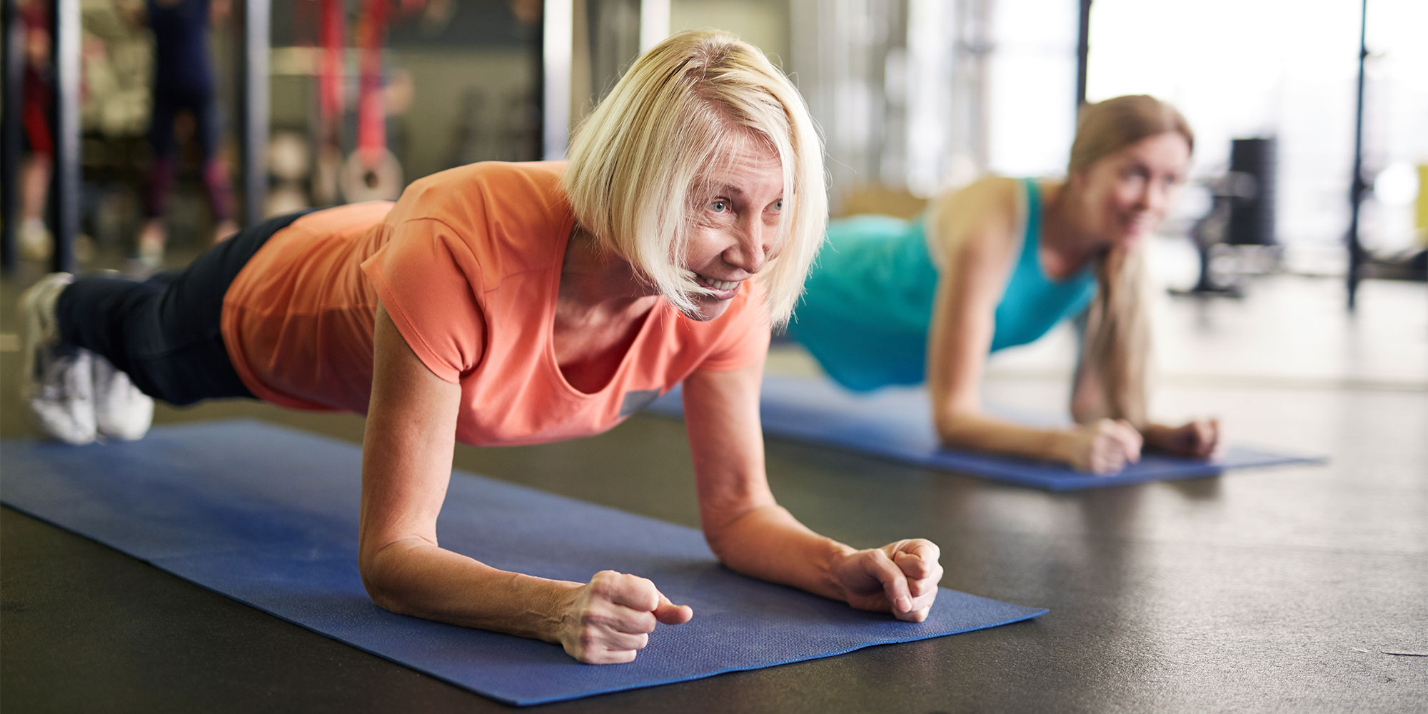 Two women holding a plank in a gym setting