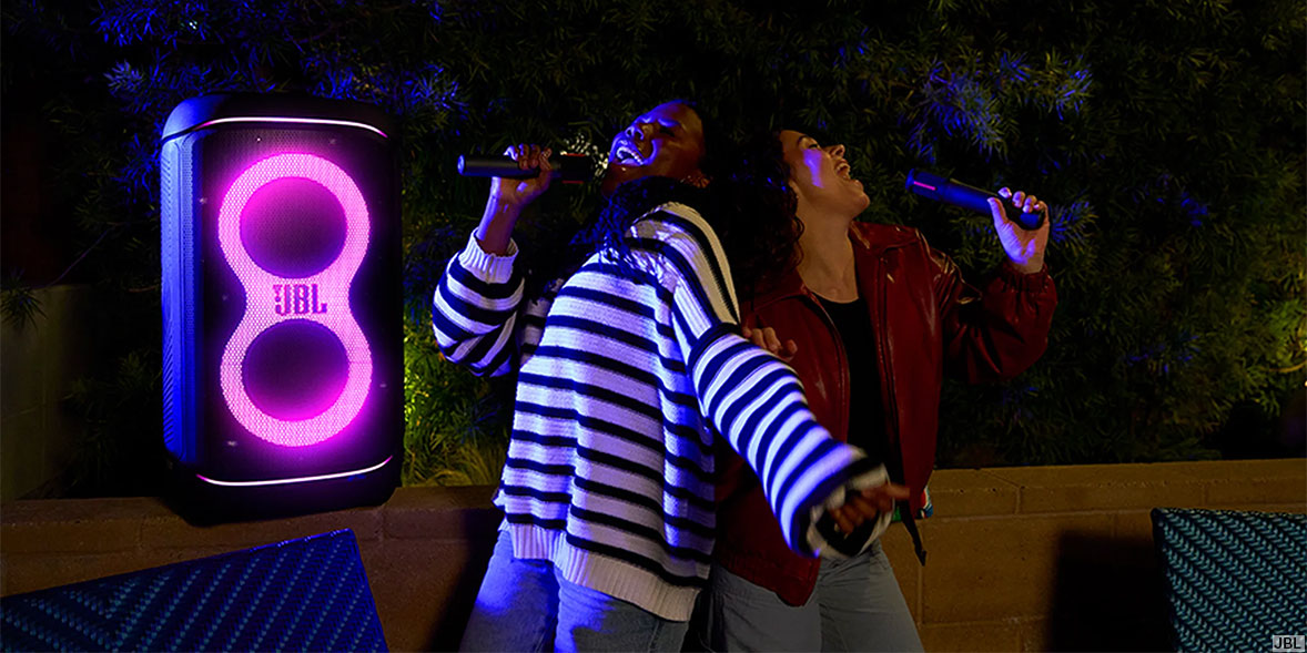A man and a woman are singing karaoke with a JBL PartyBox speaker