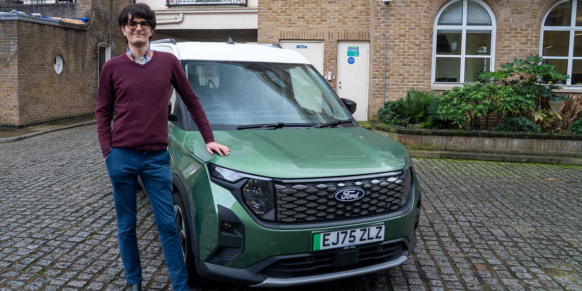 Dino Buratti stands next to a green Ford E-Tourneo Courier, parked on cobblestones