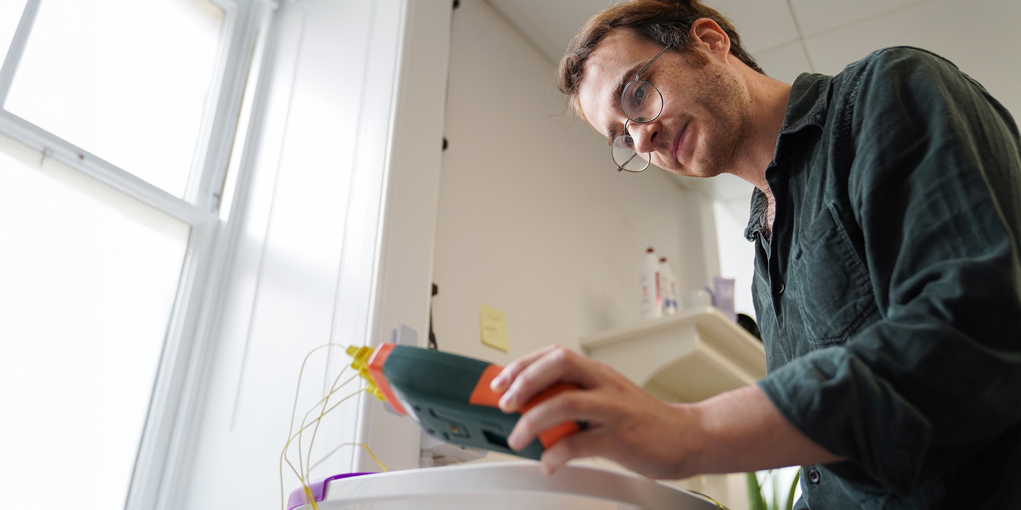 Which? expert foot spa heat retention test: tester in green shirt looking at temperature probe screen, with its probes in a foot spa