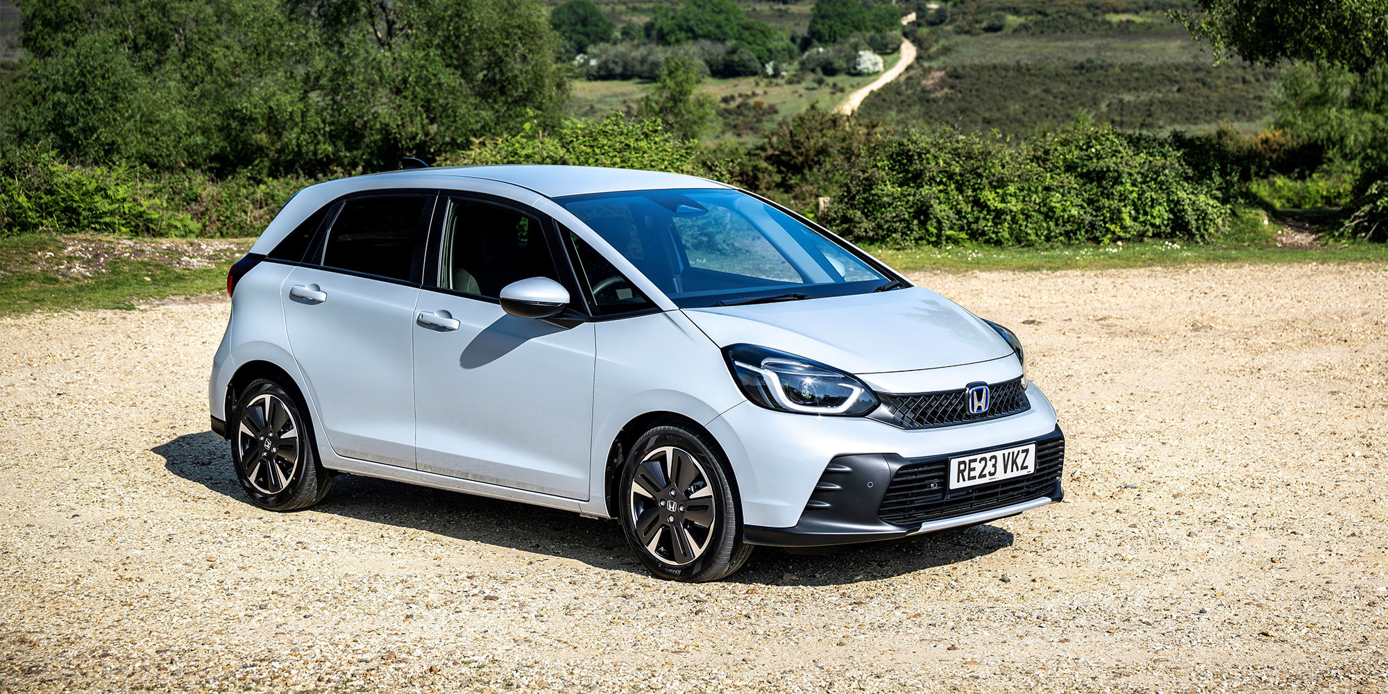 A blue Honda Jazz parked on gravel in a rural setting