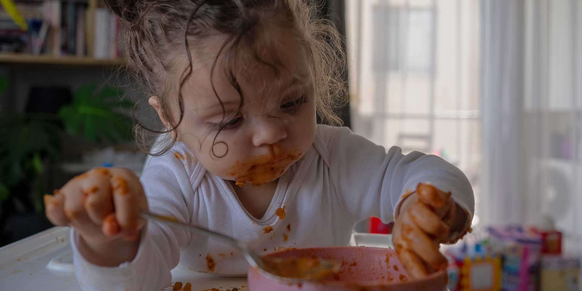 Child messily eating a bowl of pasta