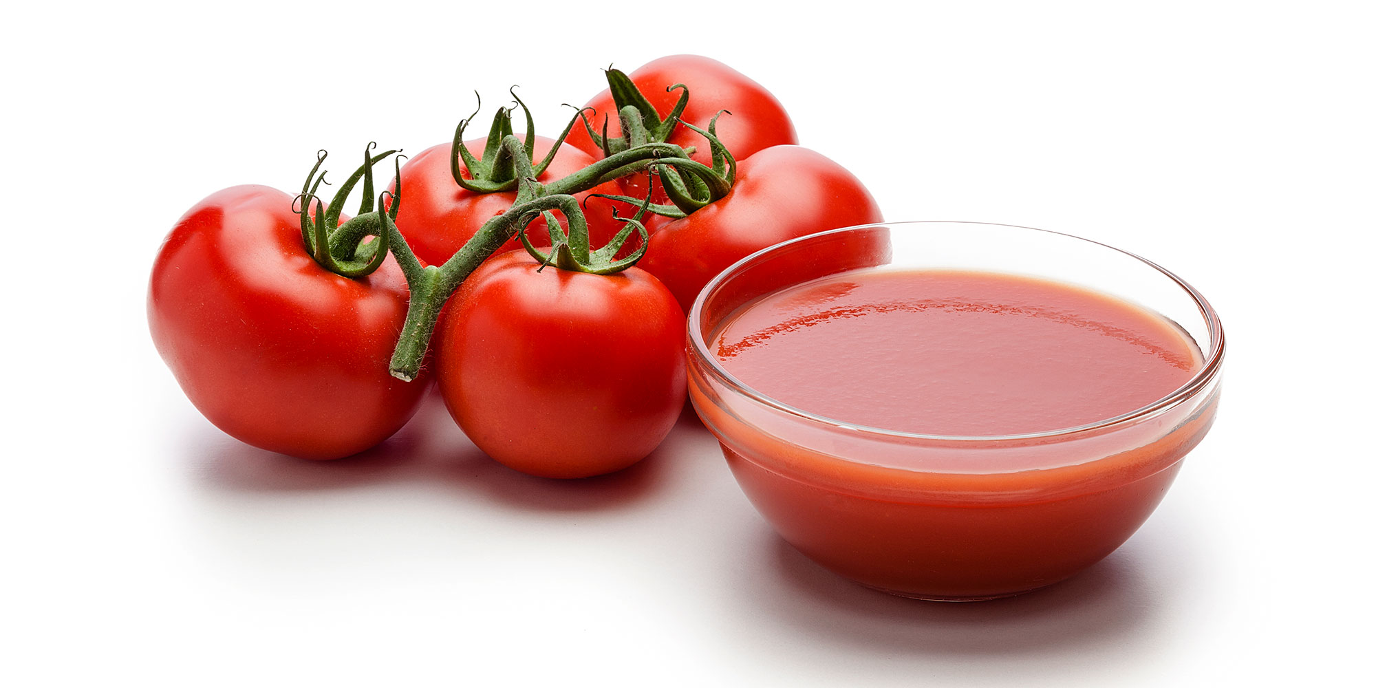 A bowl of tomato puree next to five fresh tomatoes on the vine.