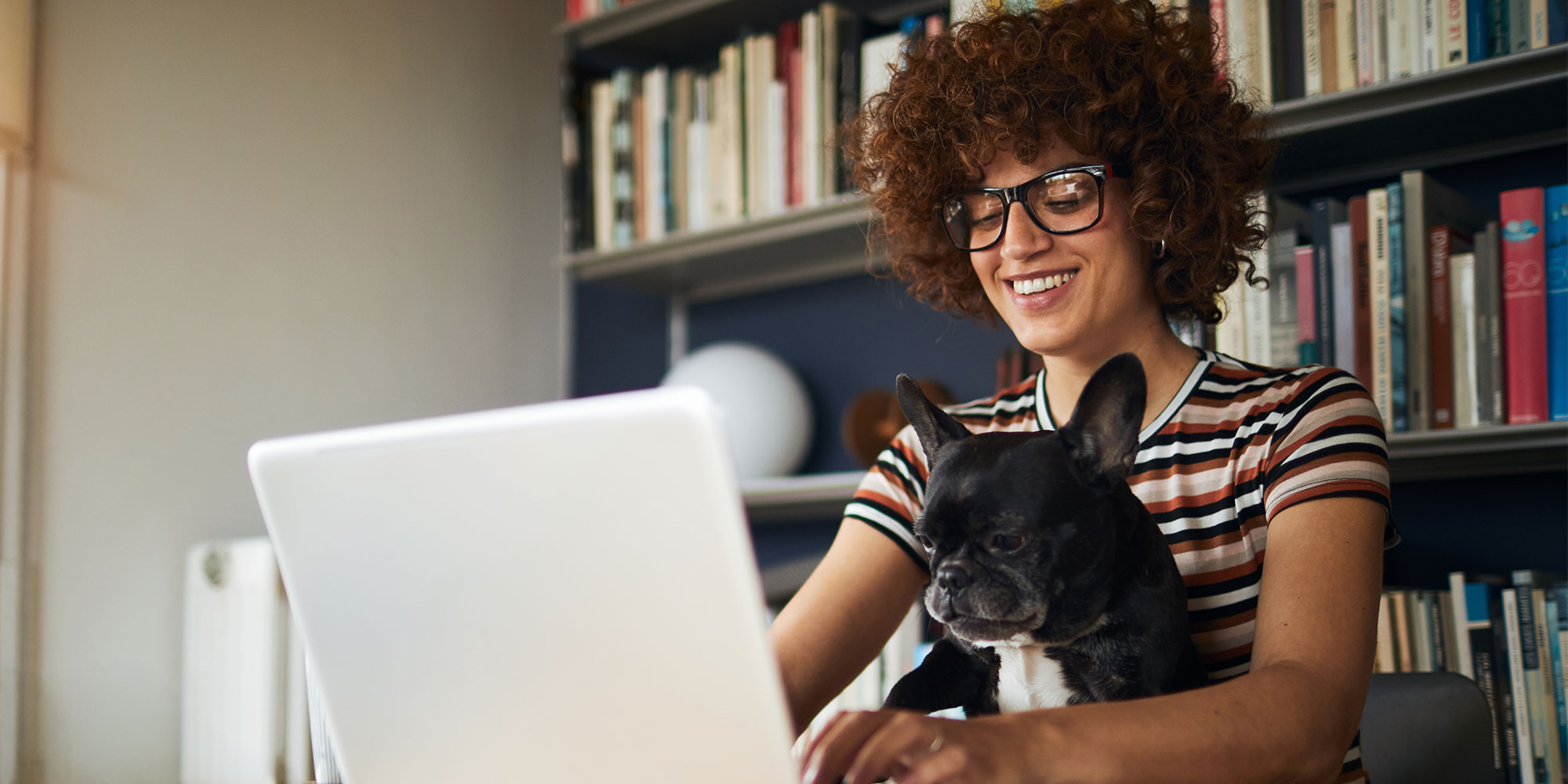 Woman looking at a laptop with a dog sitting on her lap