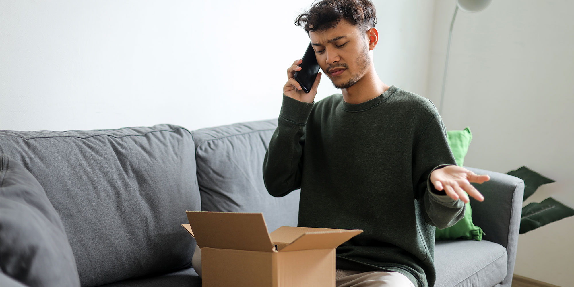 An online shopper is complaining on the phone, looking at a recently-opened parcel
