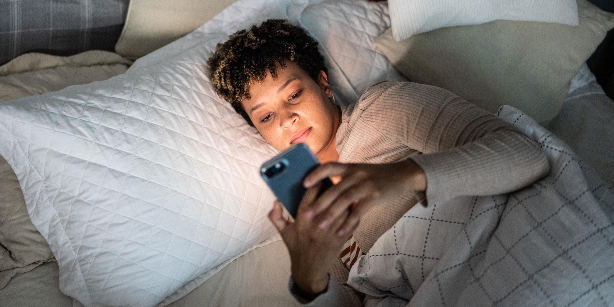 A woman in bed at night looking at her phone