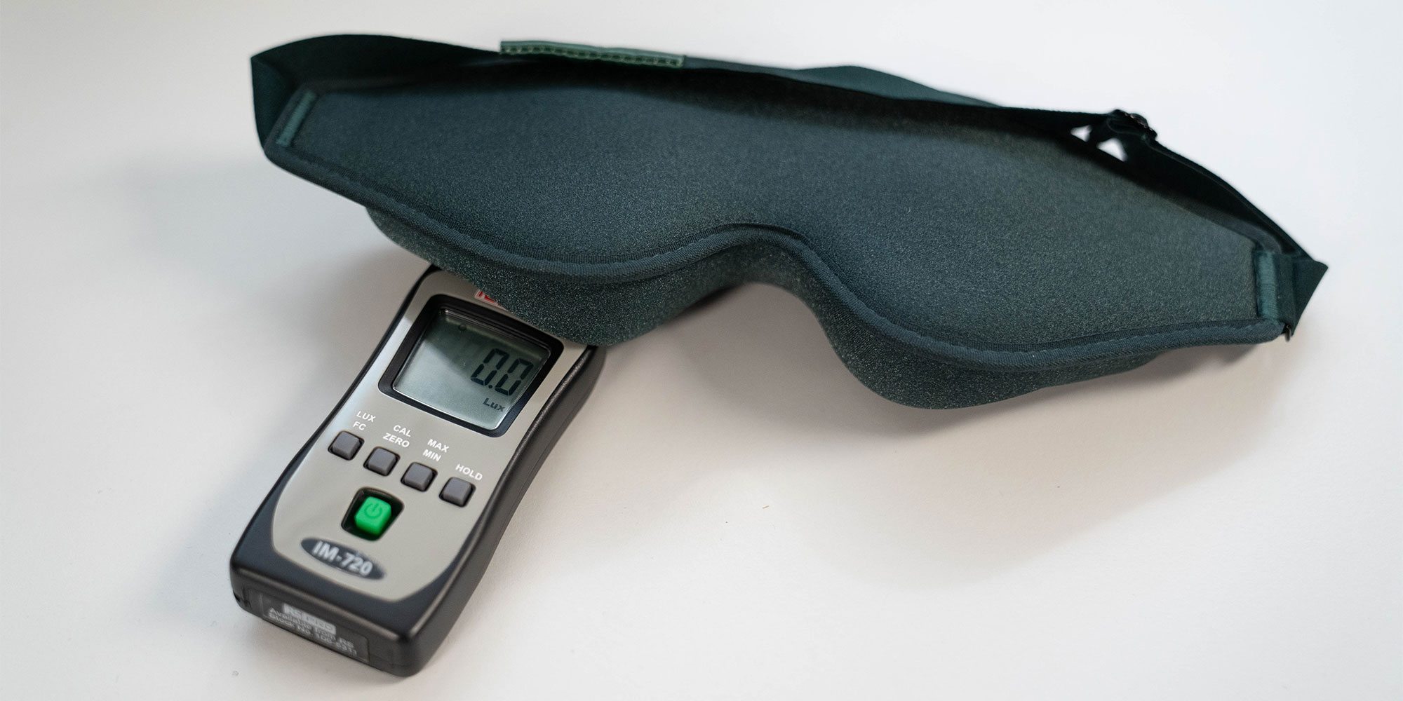 A green memory foam eye mask sitting over a digital light meter sensor