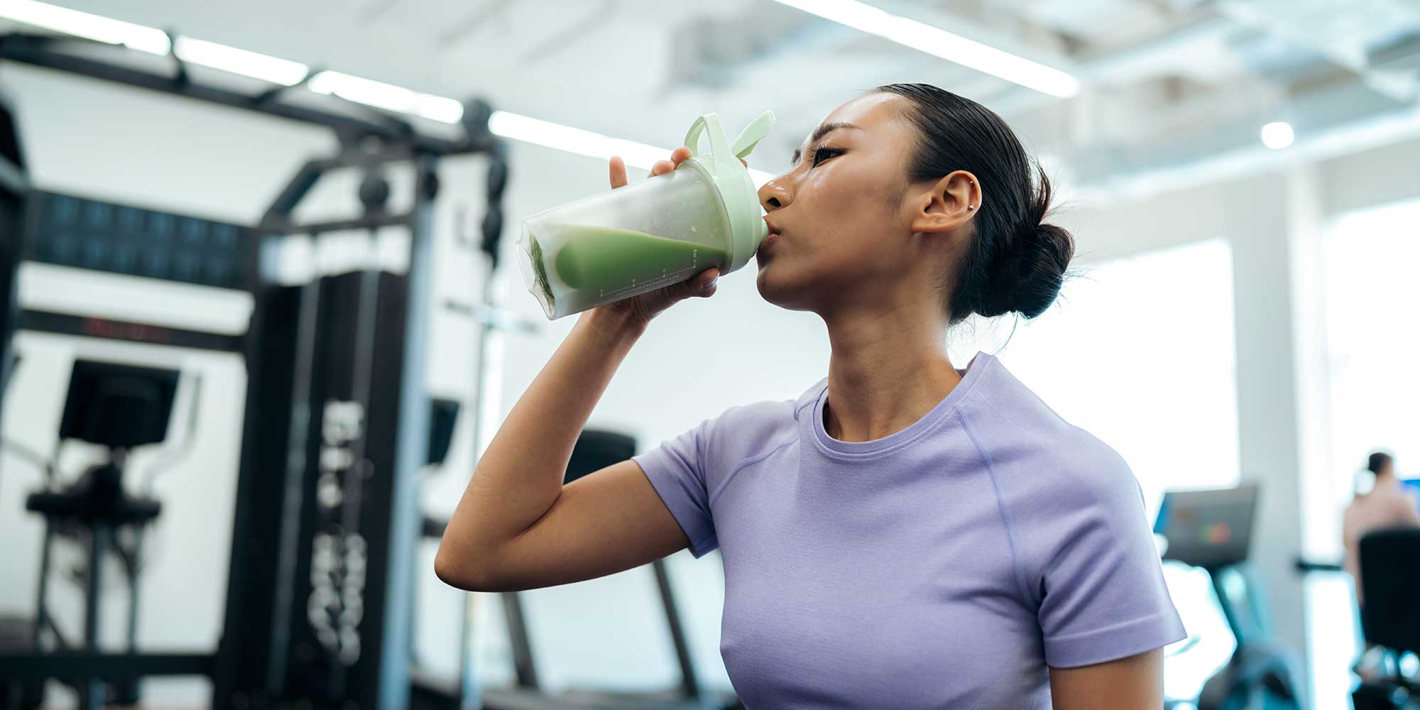 Young woman drinking a green shake at the gym