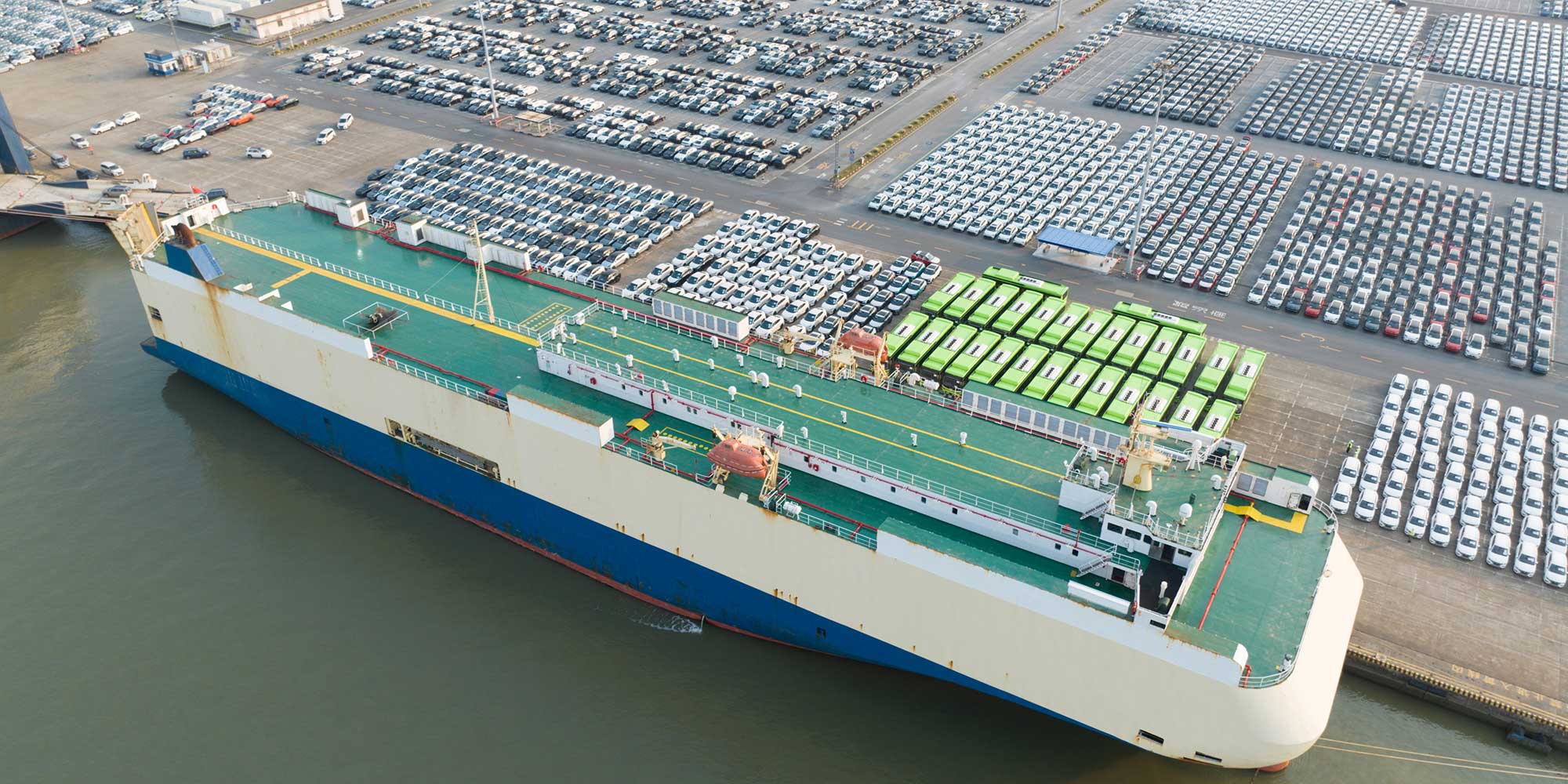 A large amount of cars parked at a dock, waiting to be loaded onto a ship.