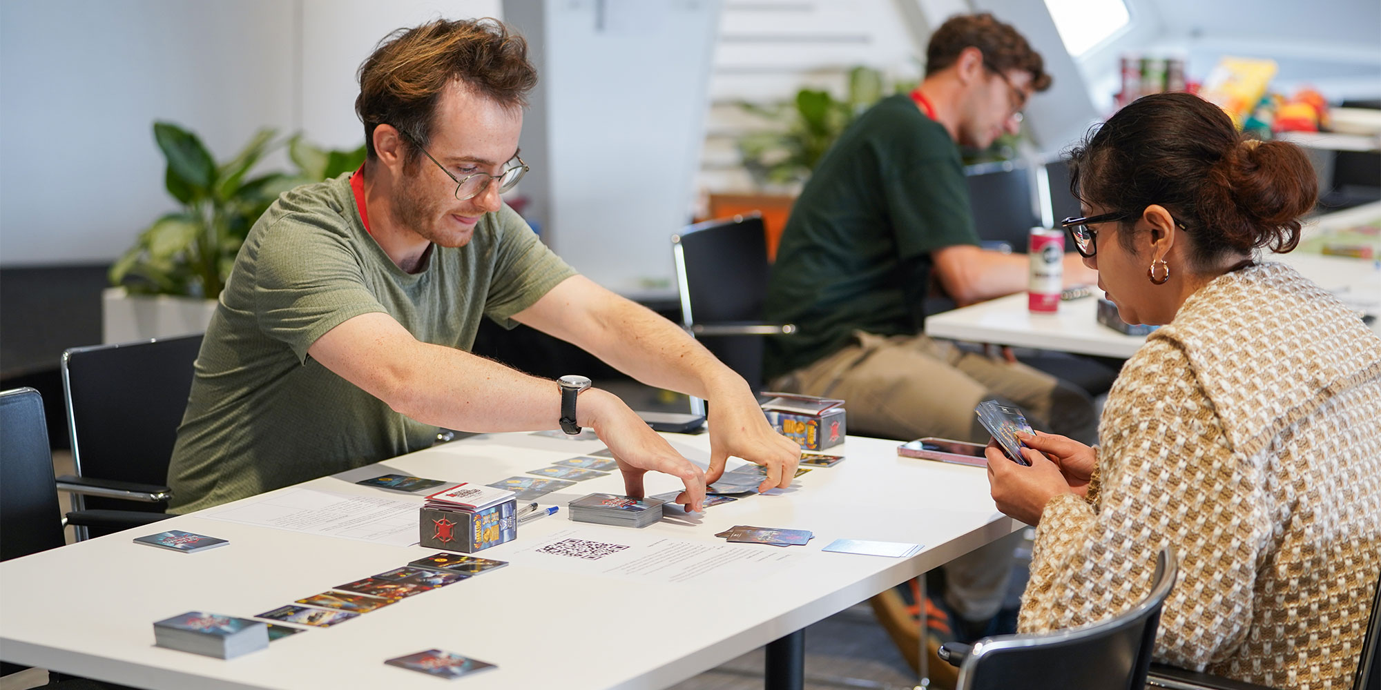 Two people at a table playing a card game. One person is wearing glasses and a green shirt.