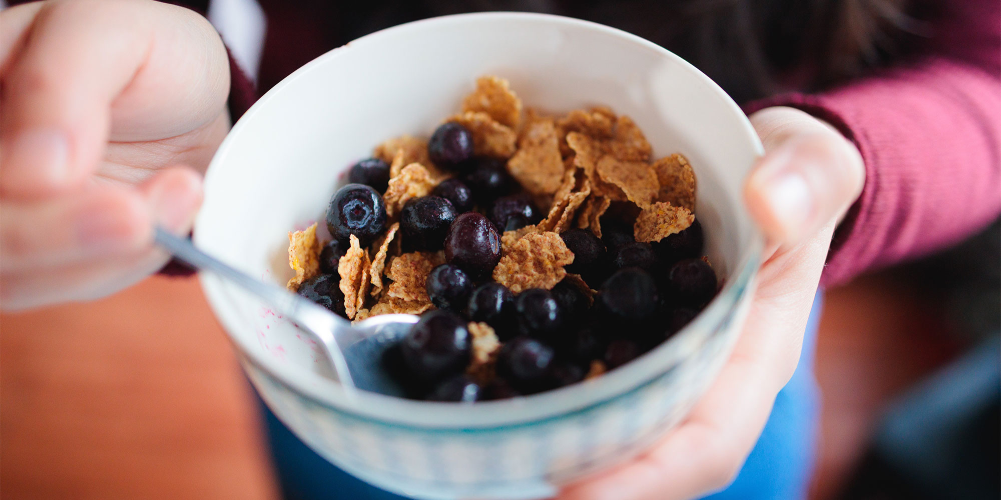 Someone putting a spoon into a bowl of blueberries and high fibre flakes.
