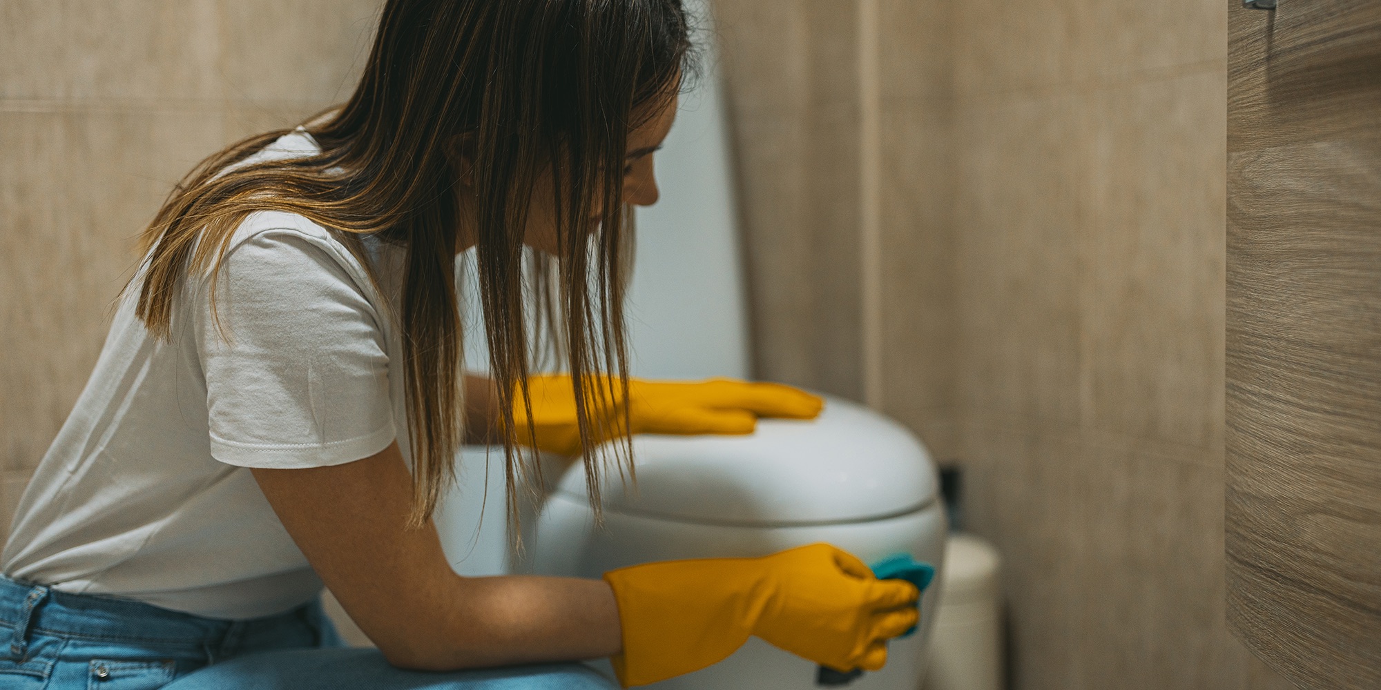 A woman wearing yellow washing-up gloves cleaning a toilet