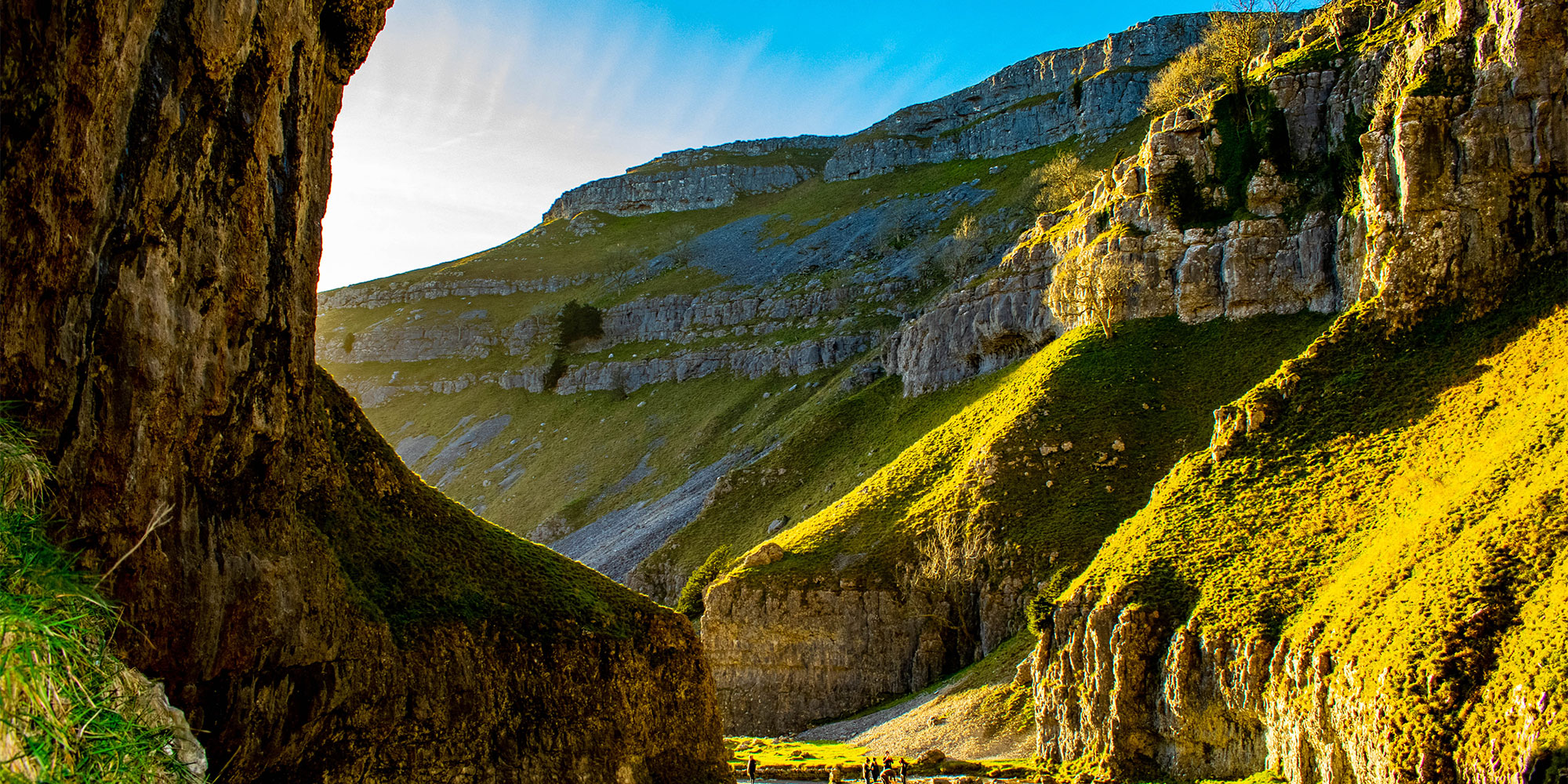 A narrow valley with steep rocky walls and a few people walking on a path.